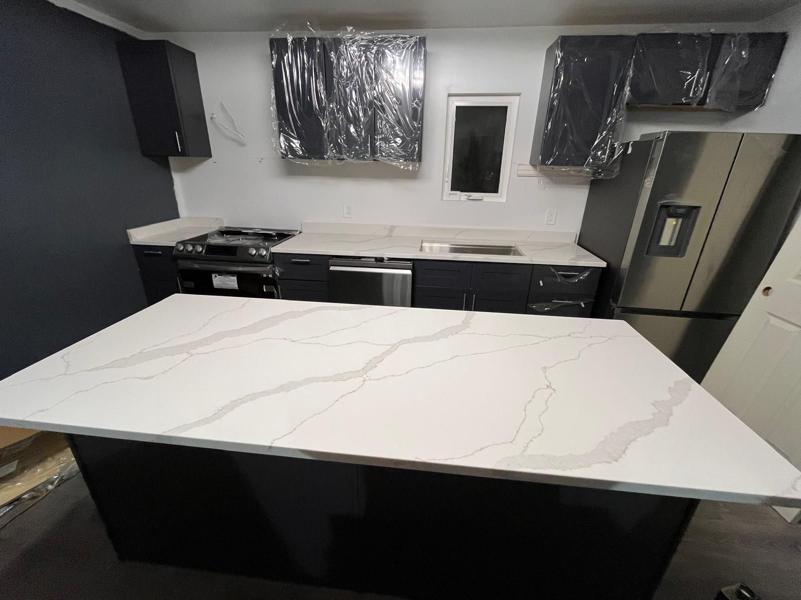 Kitchen with dark cabinets, white countertops, and stainless steel appliances. Large island in front.