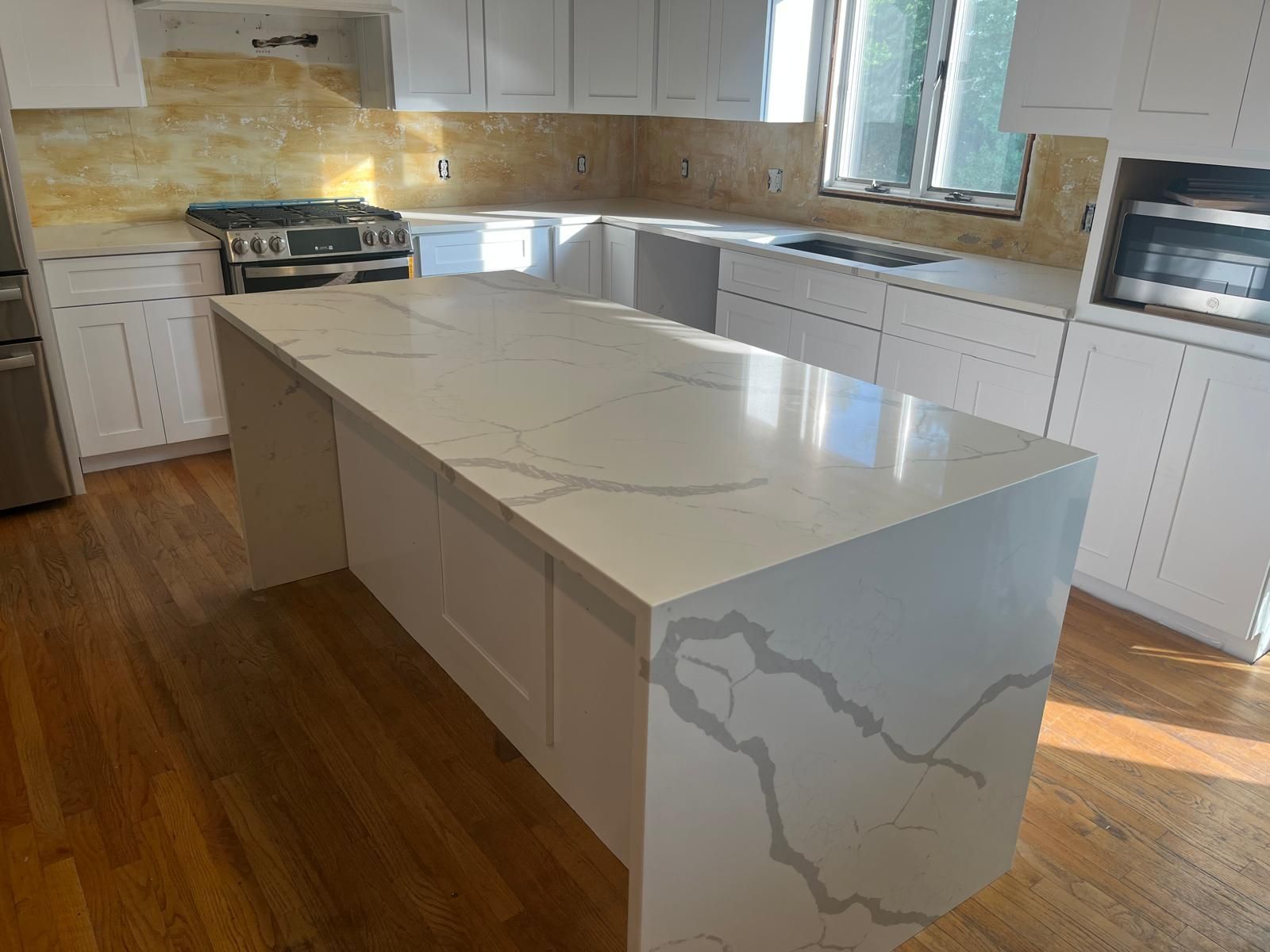 White kitchen with large island, marble countertop, wooden floor, and a gas range.