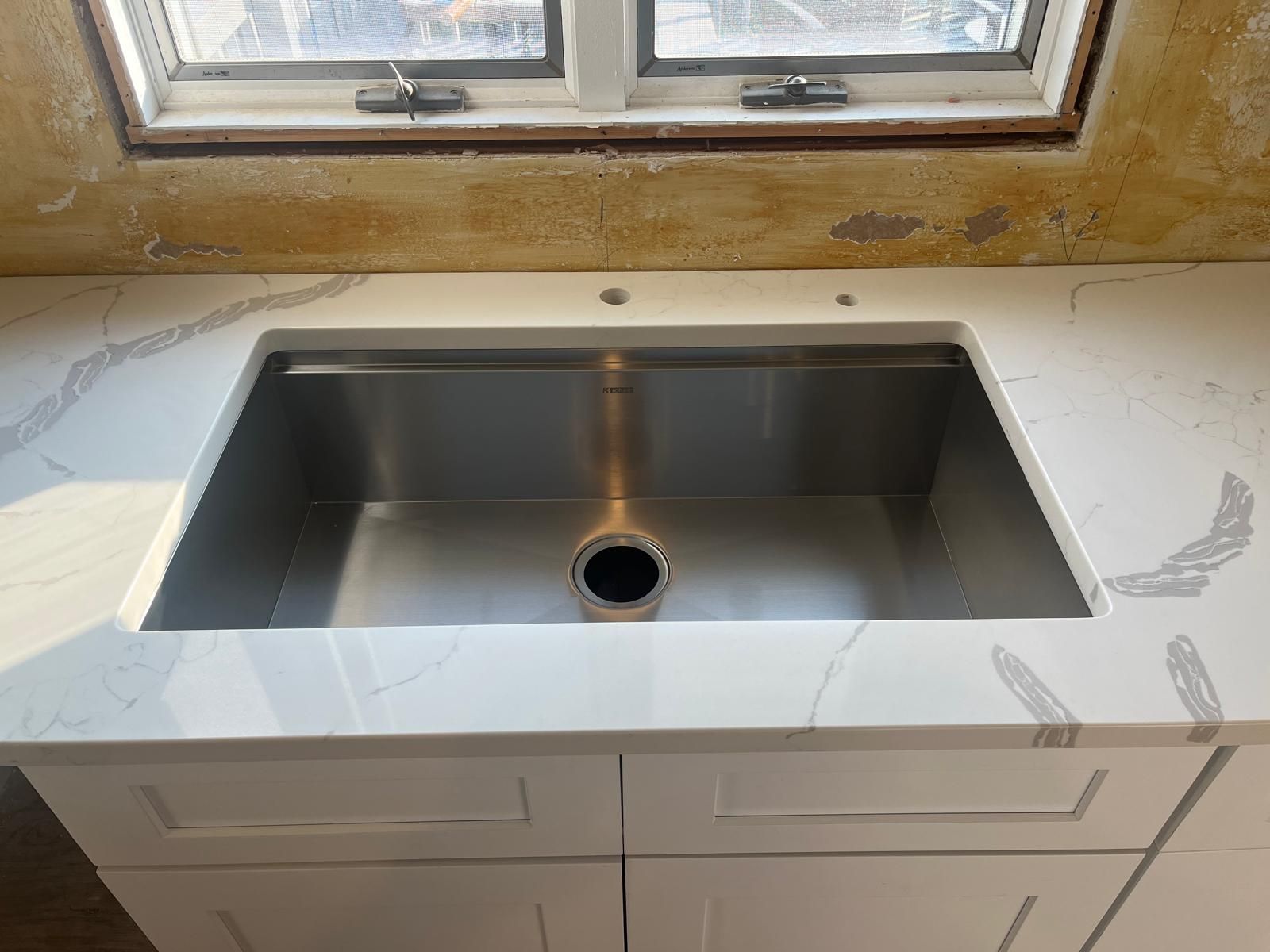 White kitchen sink installed in a countertop with a window above.