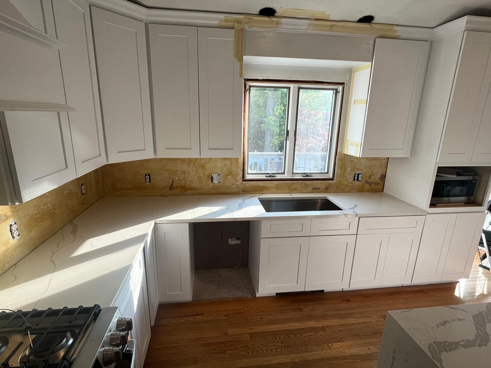 White kitchen cabinets with light-colored countertops, backsplash, and wooden floors.