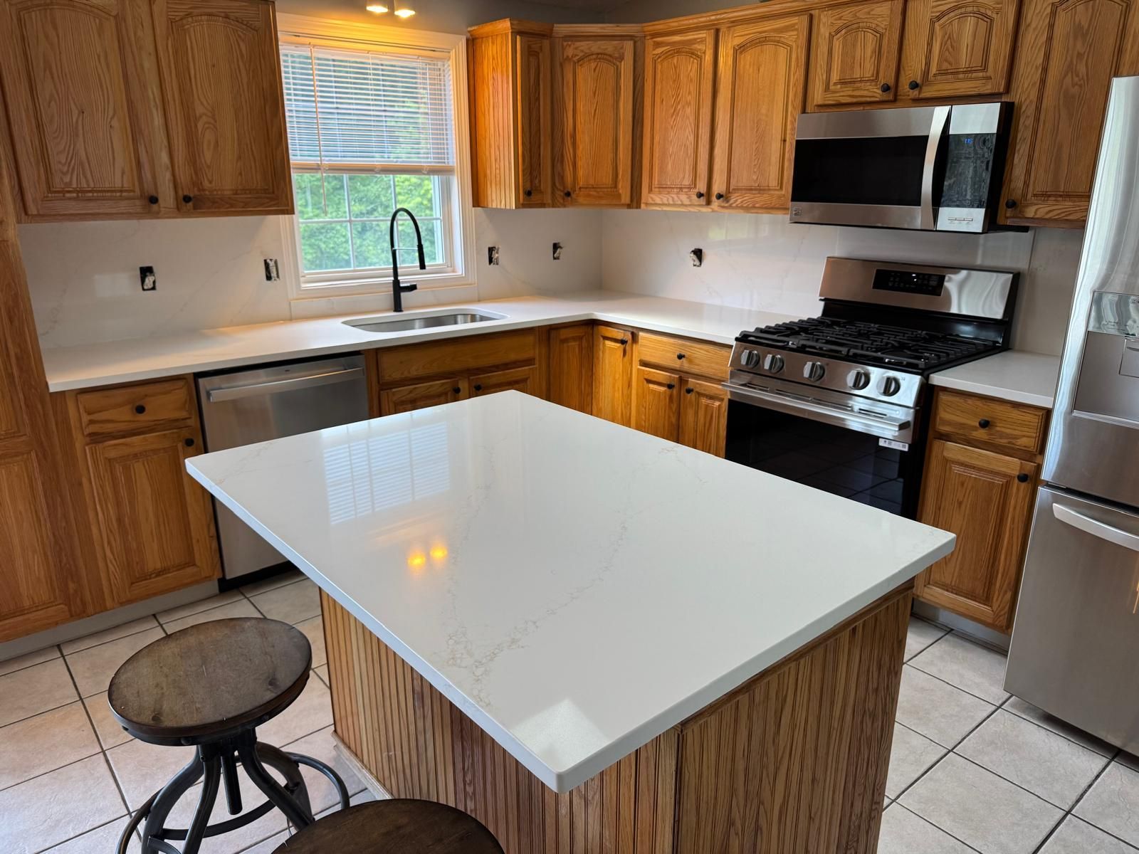 Kitchen with wooden cabinets and white countertops. Island with seating, stainless steel appliances, and sink.