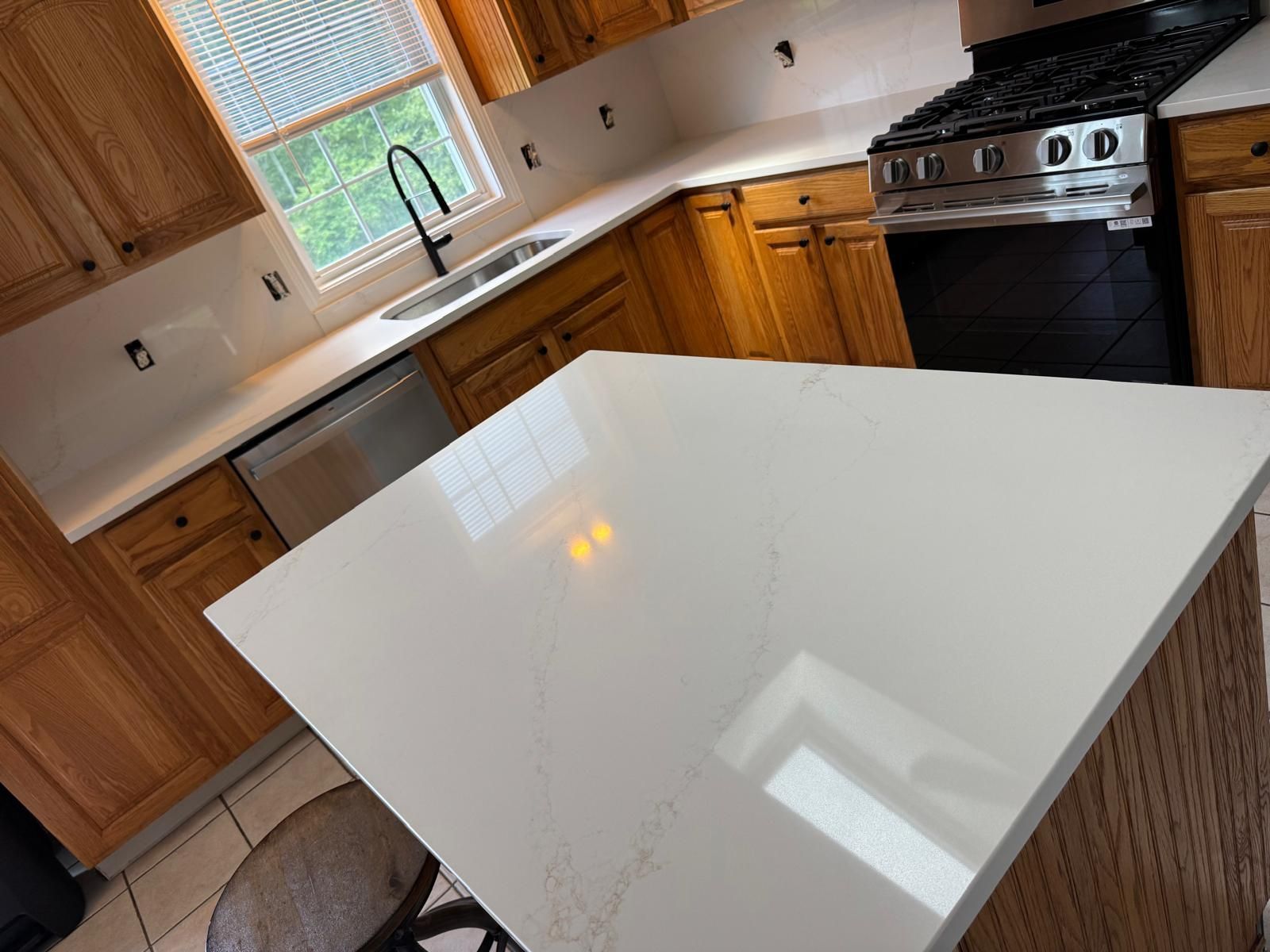Kitchen with white quartz countertops, wood cabinets, black faucet, and stainless steel appliances.
