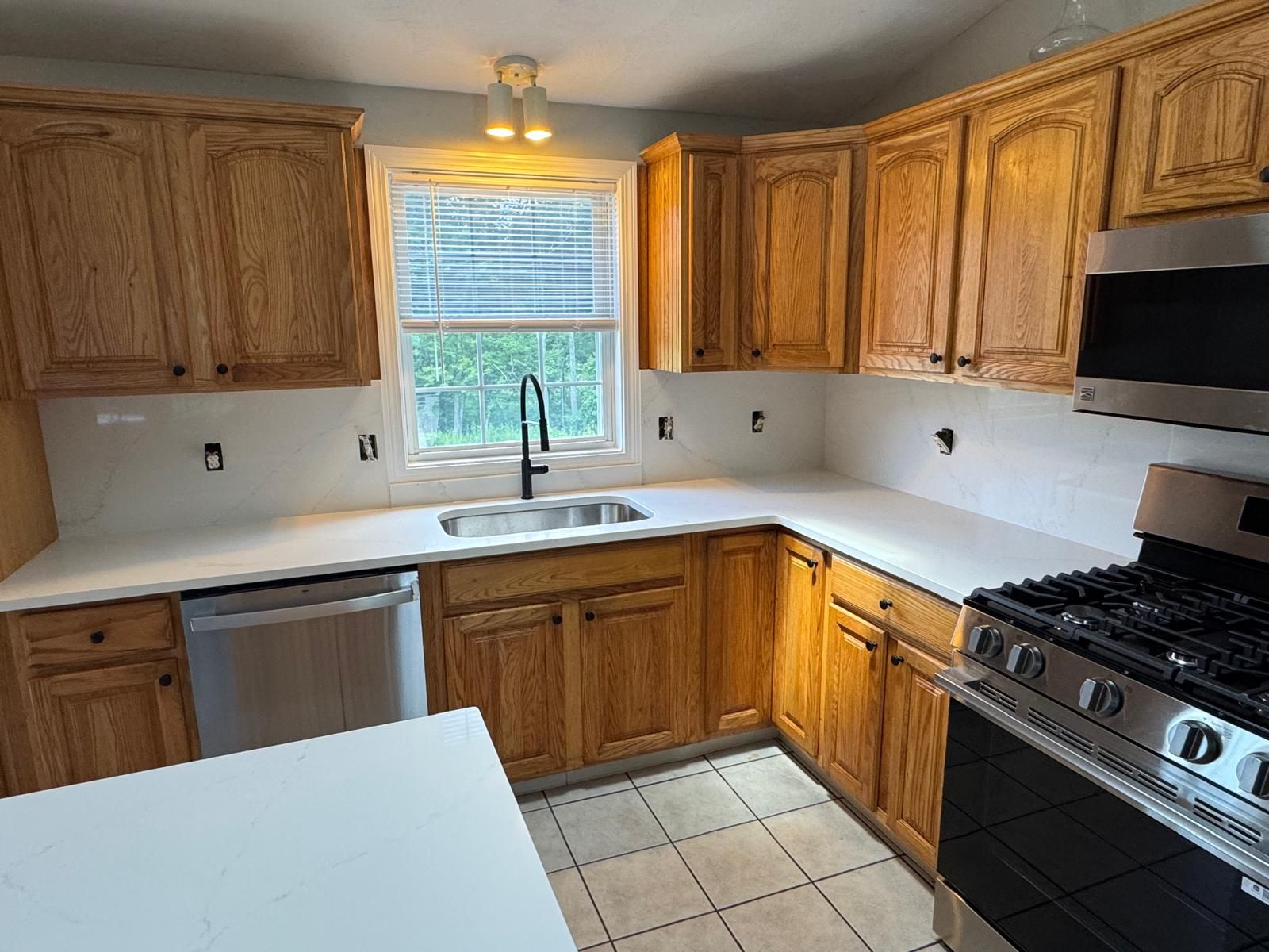 Kitchen with light wood cabinets, white countertops and backsplash, stainless steel appliances, and a window.