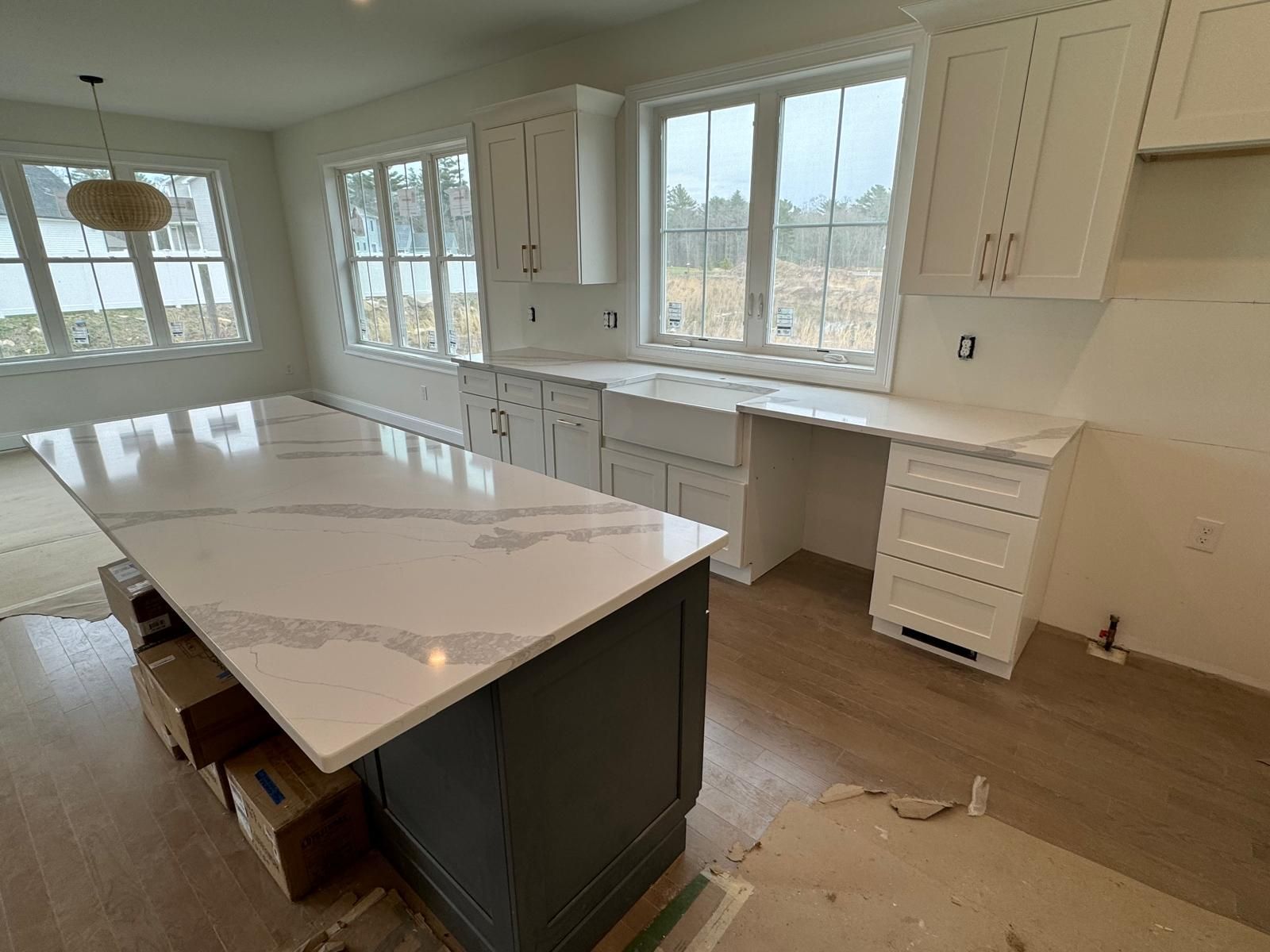A kitchen with white cabinets, a large island with a quartz countertop, and light wood flooring.