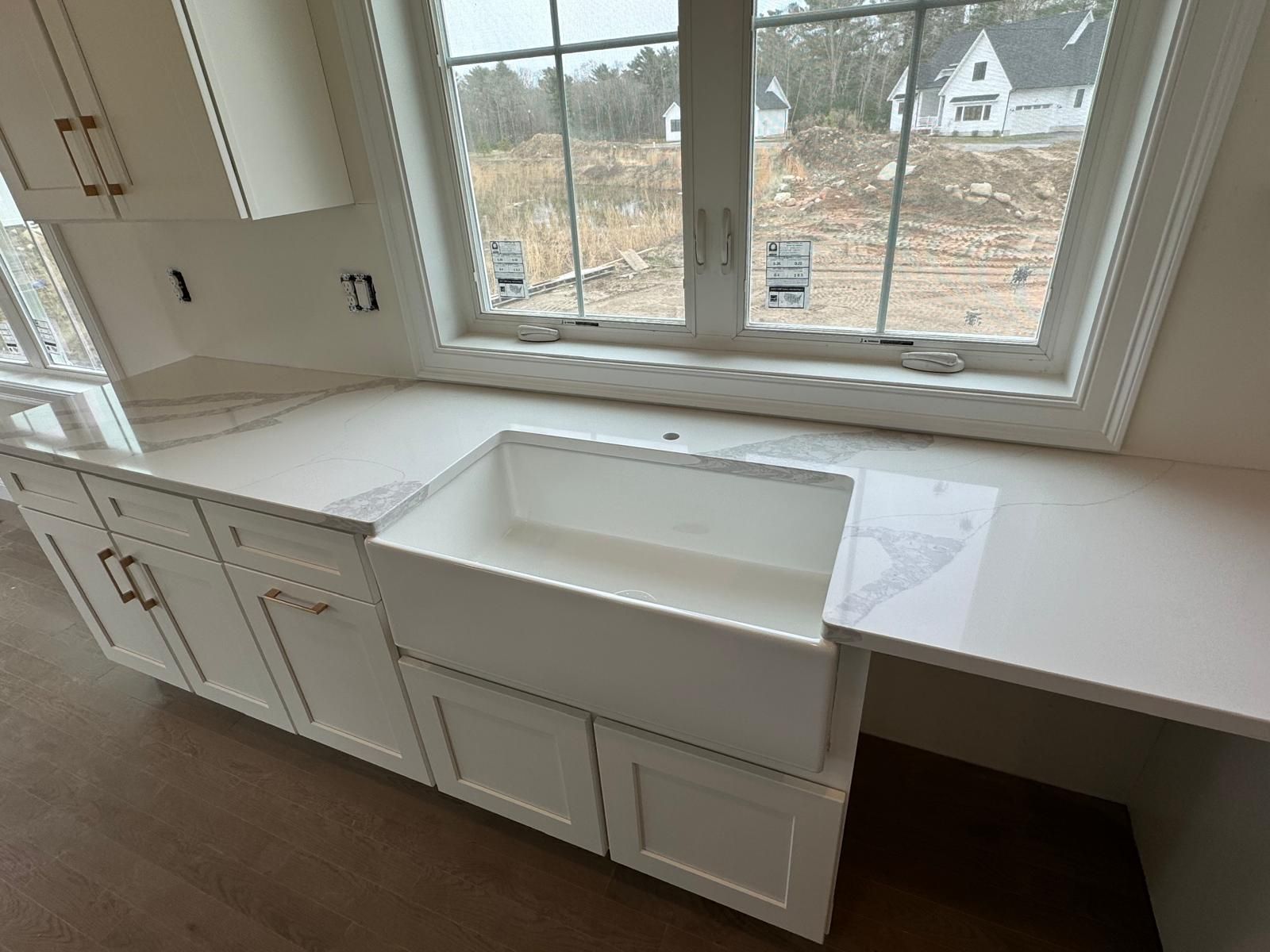 Kitchen with white cabinets, farmhouse sink, and large window overlooking construction site.