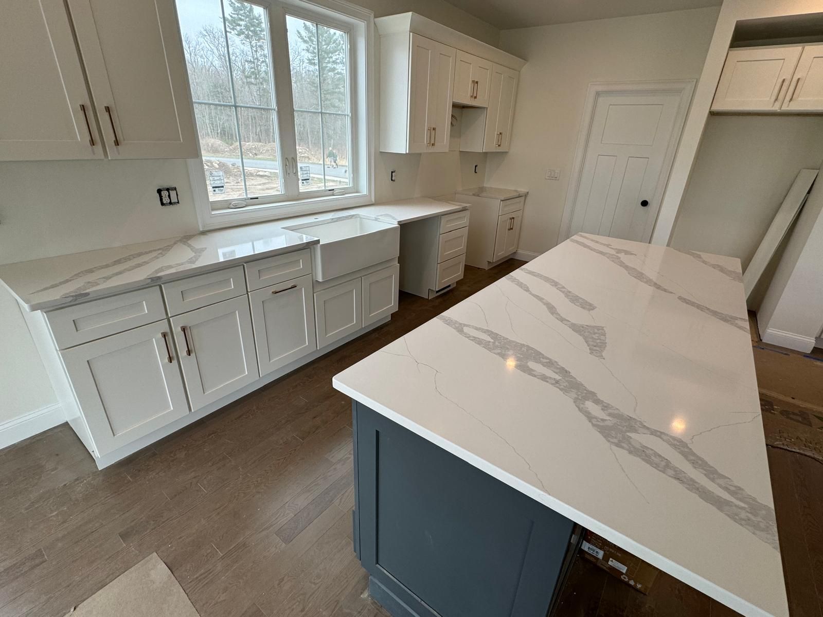 White kitchen with quartz countertops and a dark blue island.