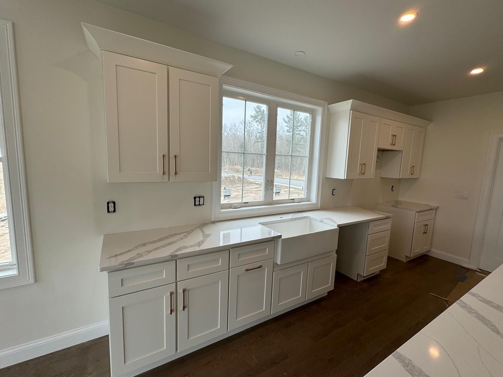 White kitchen with cabinets, countertops, and a farmhouse sink, next to a window.