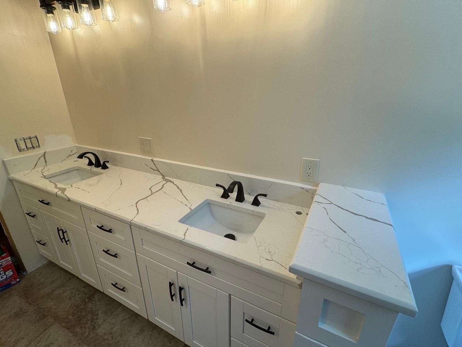White bathroom vanity with two sinks, black fixtures, and marble-like countertop against a white wall.