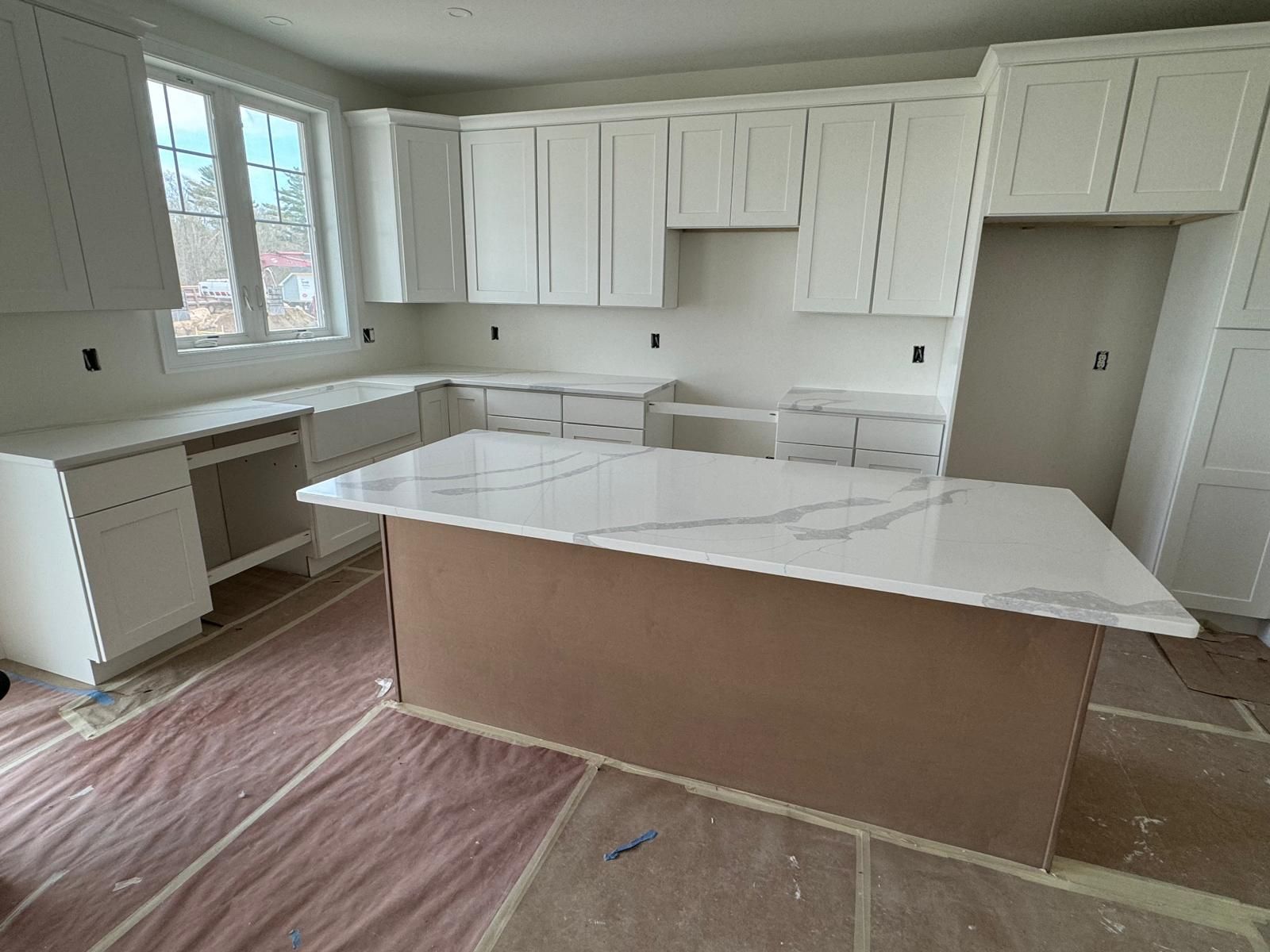 White kitchen cabinets and island with light countertop, under construction.