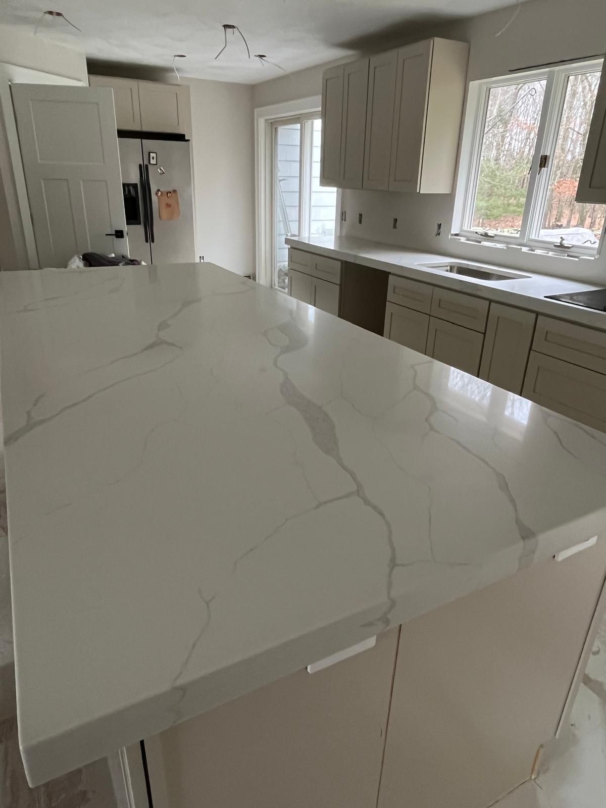 A kitchen with a large white countertop island and cabinets.
