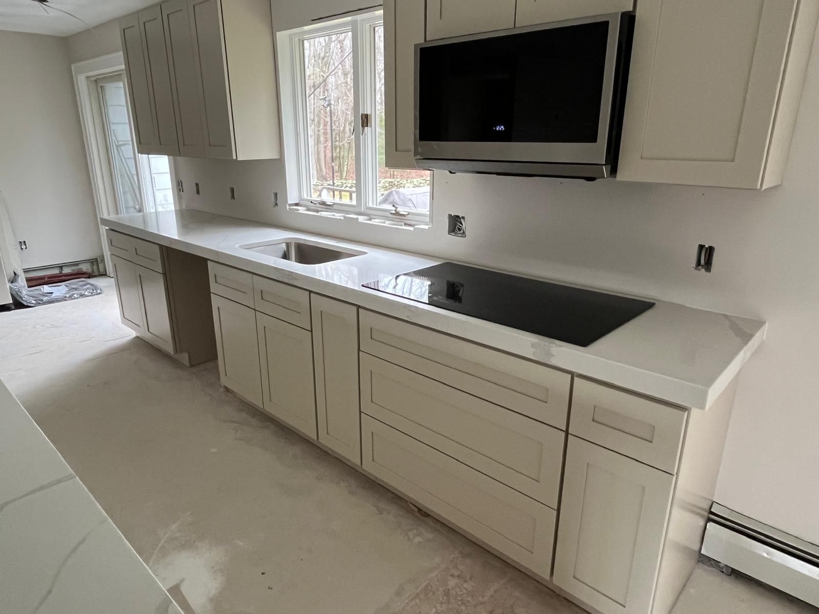 Cream-colored kitchen cabinets and counters. Includes sink, cooktop, microwave, and window.