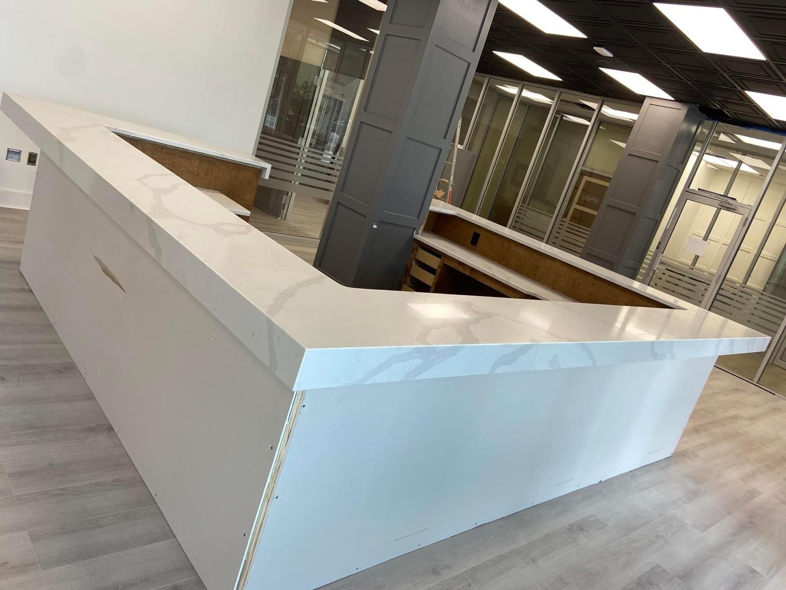 White quartz countertop on a white rectangular bar in an office space with glass walls.