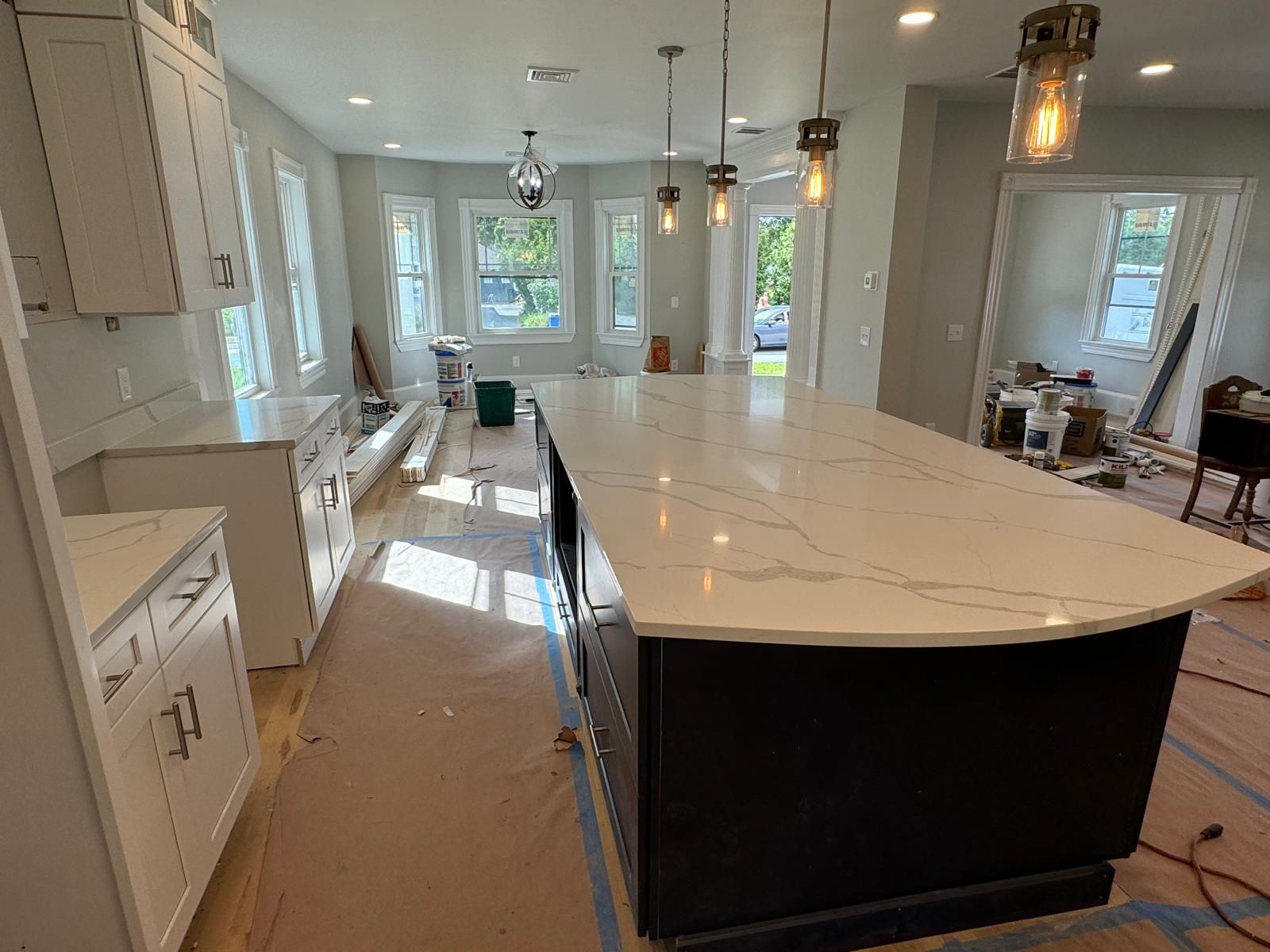 Kitchen under construction; white cabinets, dark island with white countertop, windows in background.