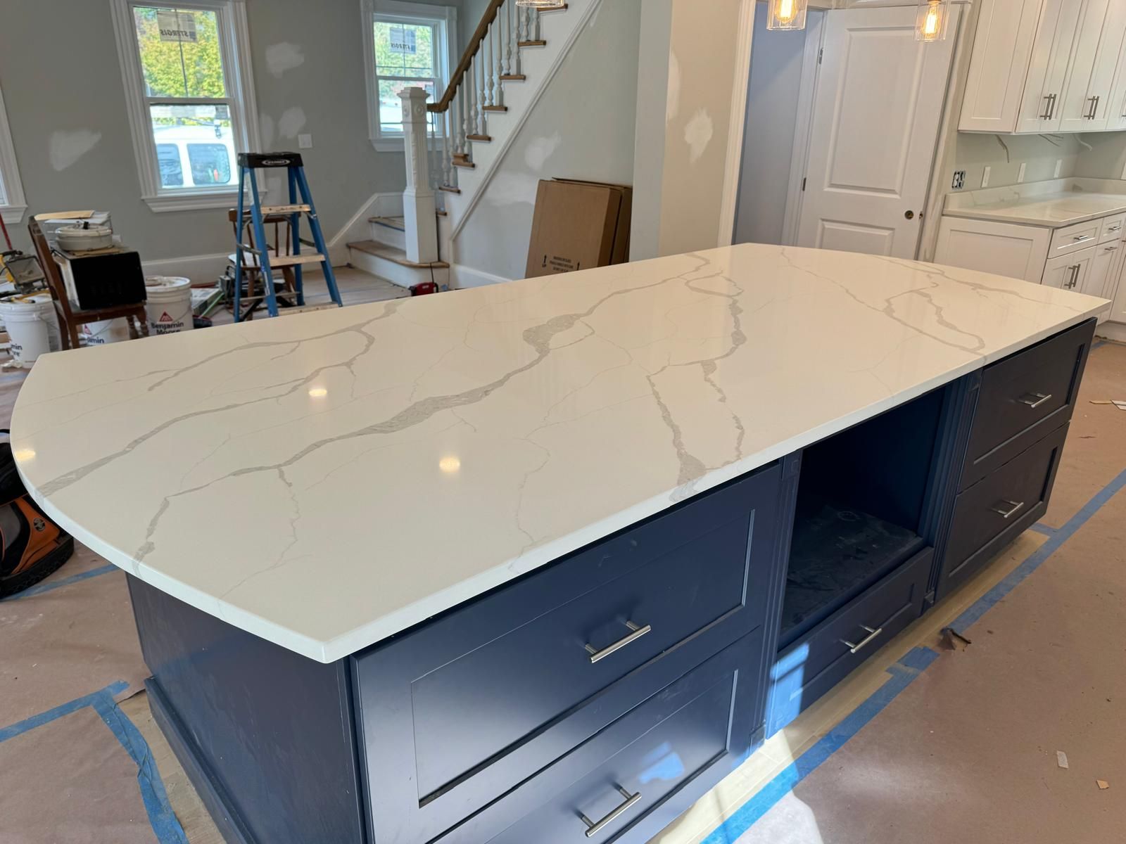 Kitchen island with white marble-look countertop and navy blue cabinets. Drawers and open space below.