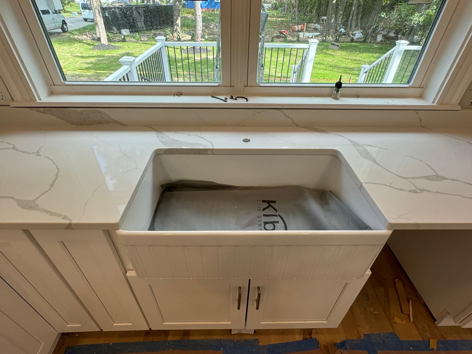 White kitchen sink set in white countertop under a window, with white cabinets below.