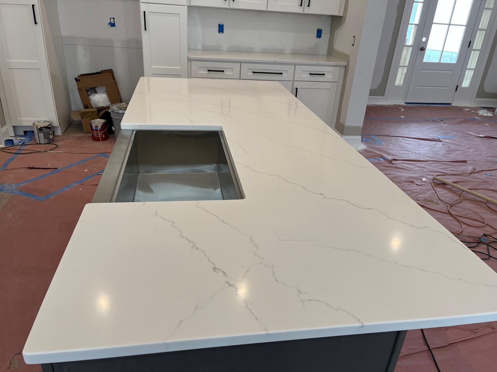Kitchen island with white countertops, sink, and cabinets; construction in progress.