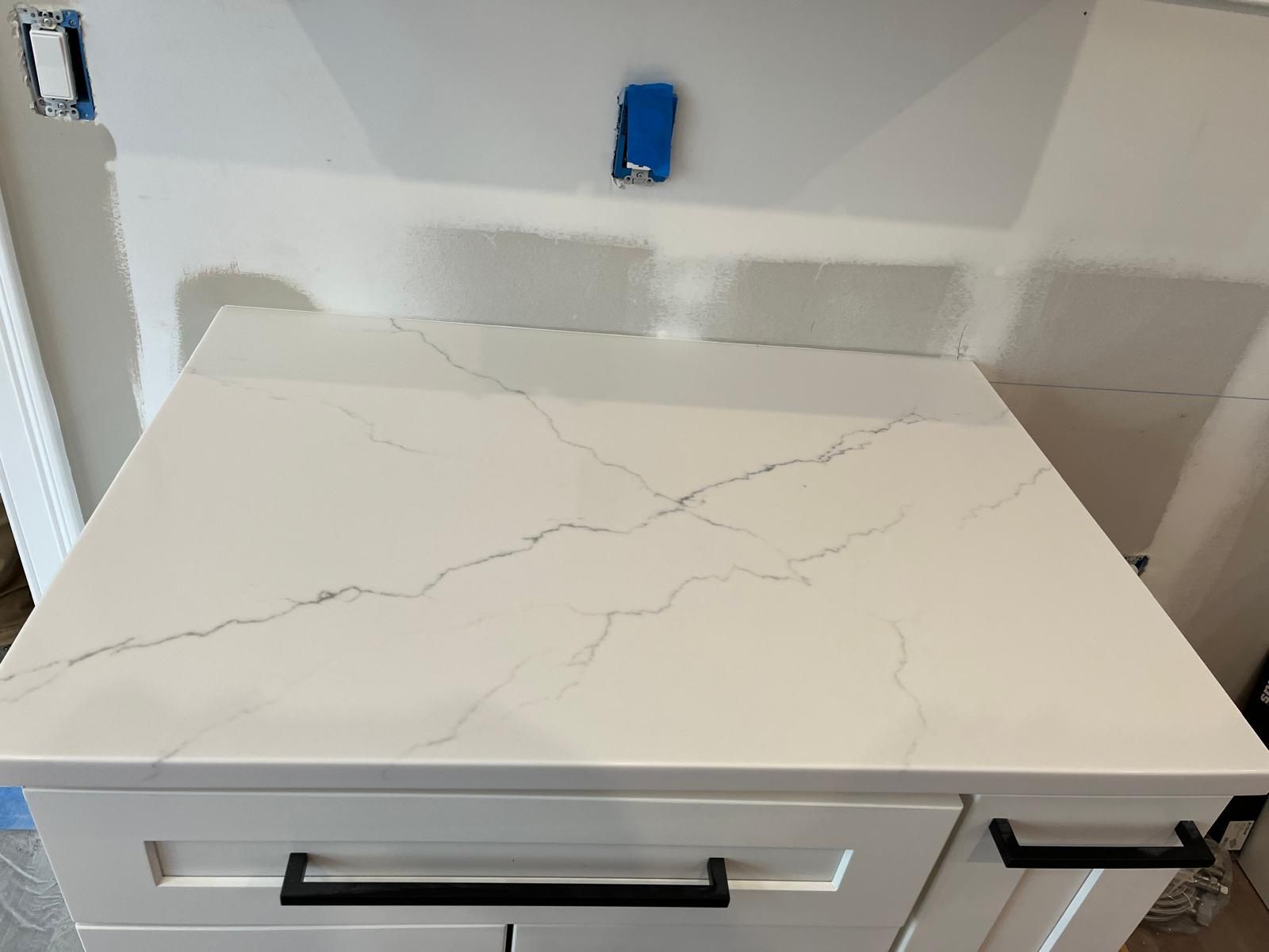 White quartz countertop with black veining, on a white cabinet with black handles.