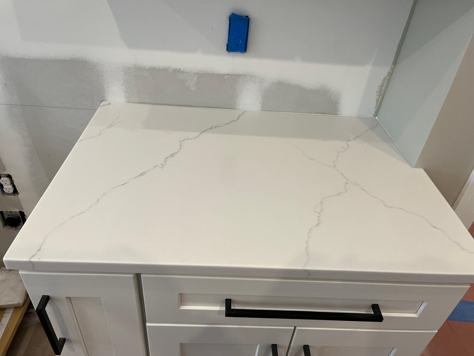 White quartz countertop on a white cabinet with black handles against a wall.