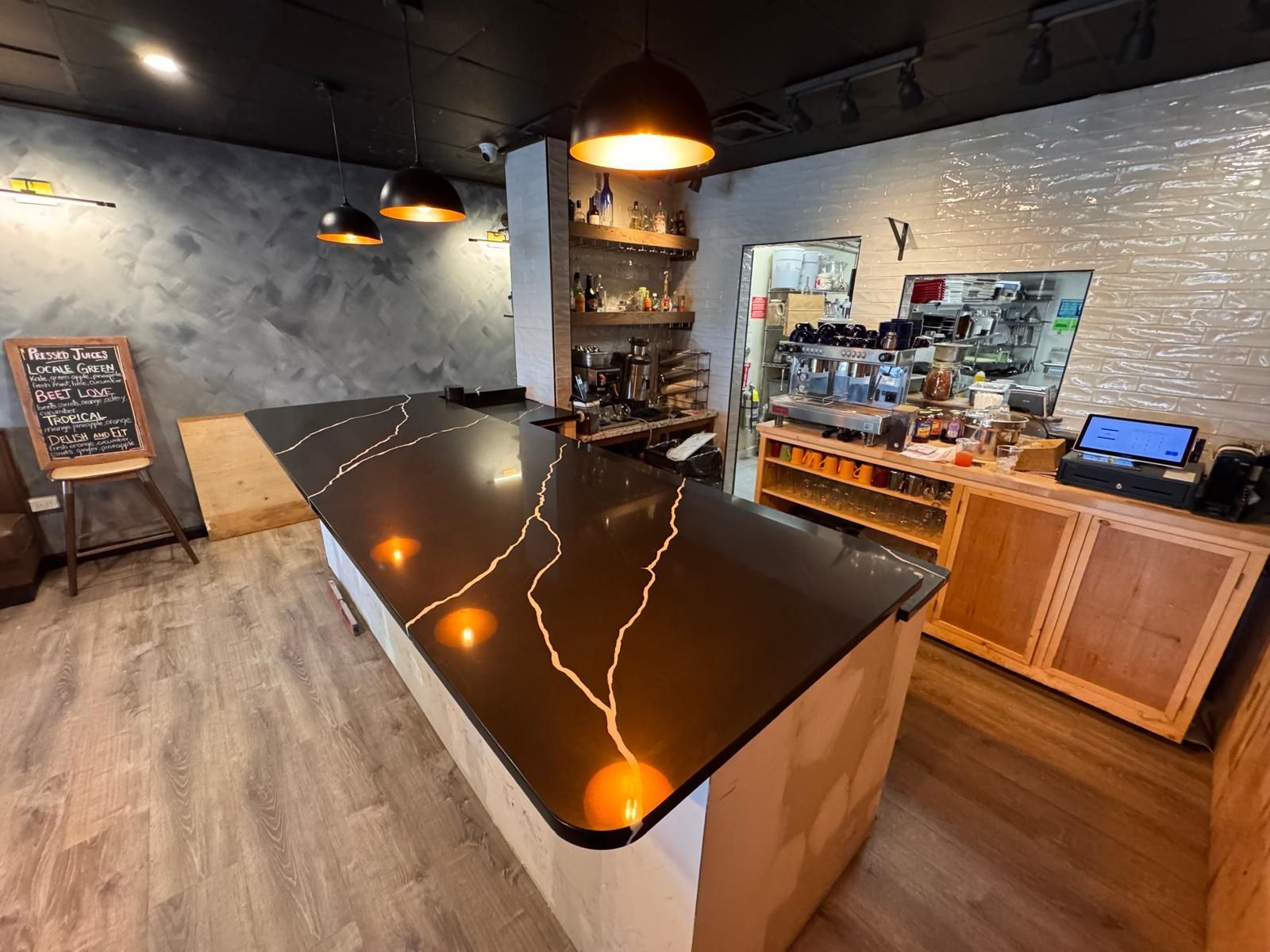 Coffee shop interior with black countertop, pendant lights, wooden shelves, and espresso machines.