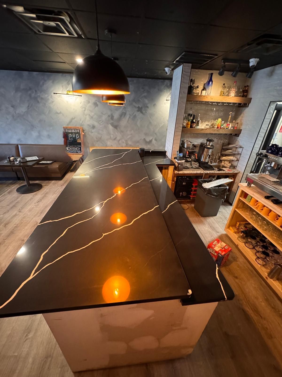 Black countertop with gold veining in a bar; shelves of liquor and a black ceiling.