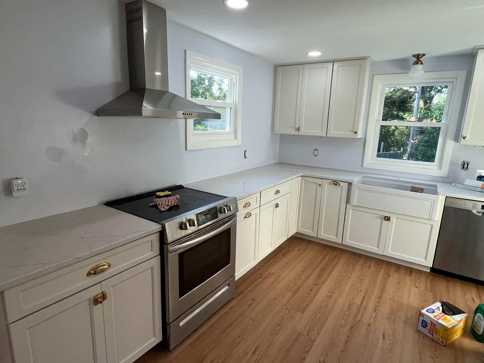 A bright kitchen with white cabinets, stainless steel appliances, light countertops, and wood flooring.