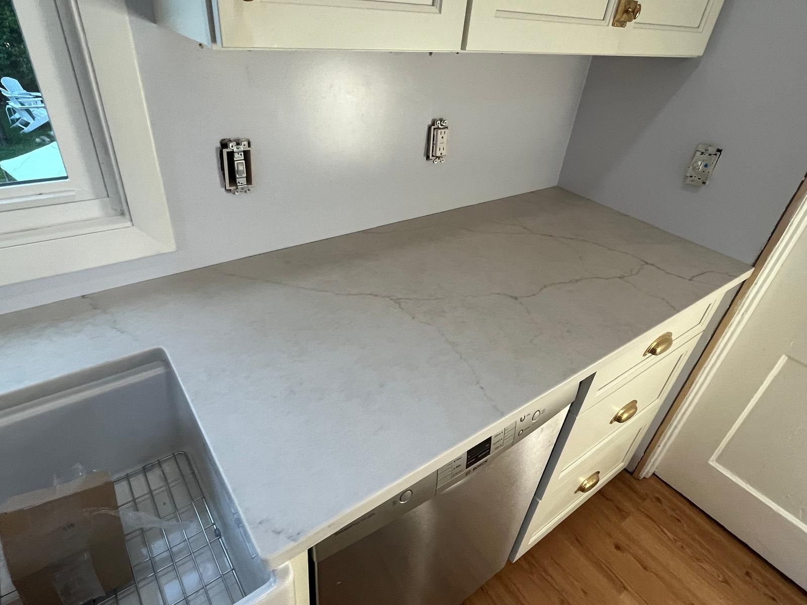 Kitchen with white cabinets, light gray countertop, stainless steel dishwasher, and a window.