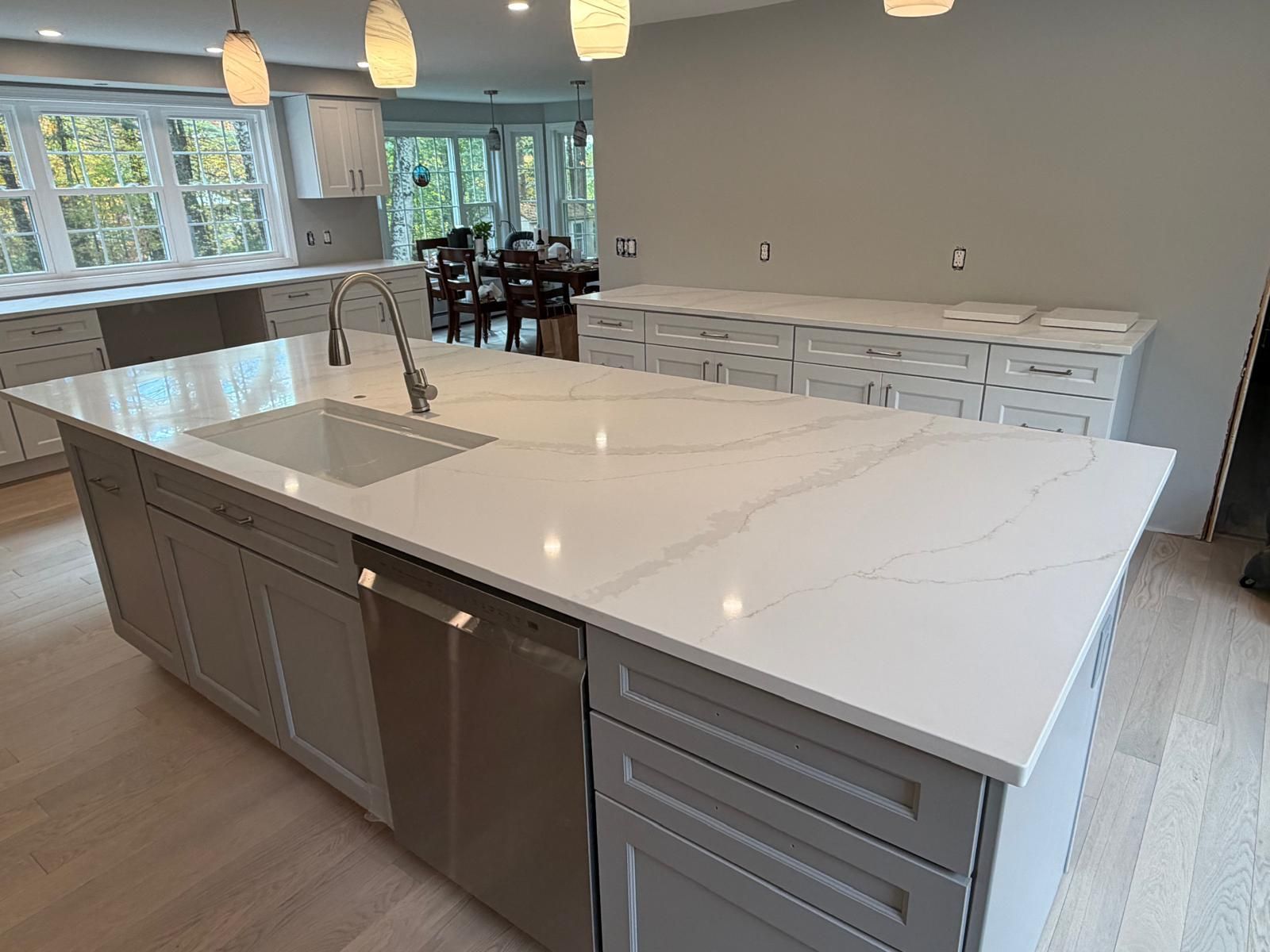 Newly remodeled kitchen featuring a large island with a sink, dishwasher, and white countertops.