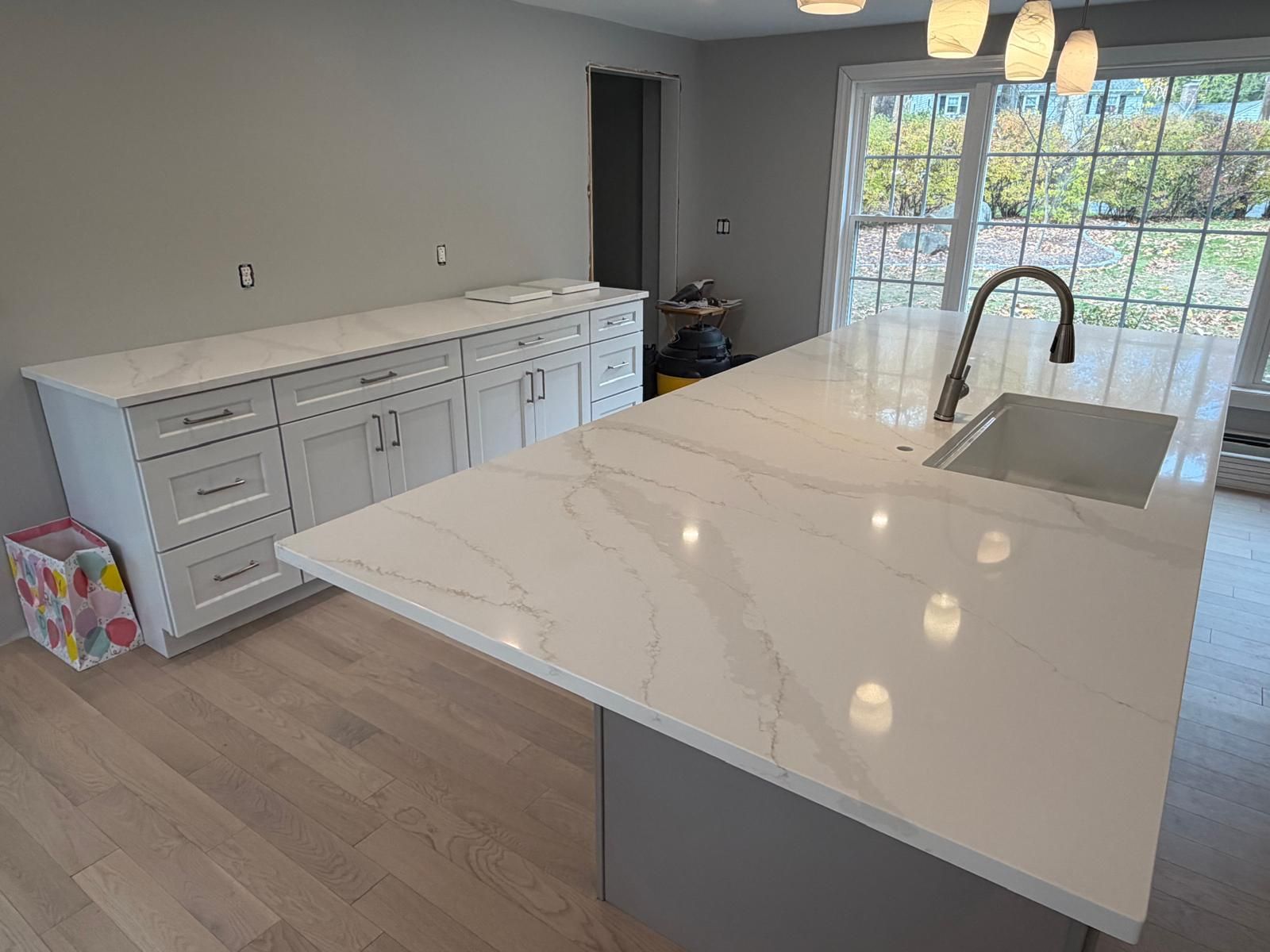Kitchen with white cabinets, quartz countertops, and a large island with a sink.