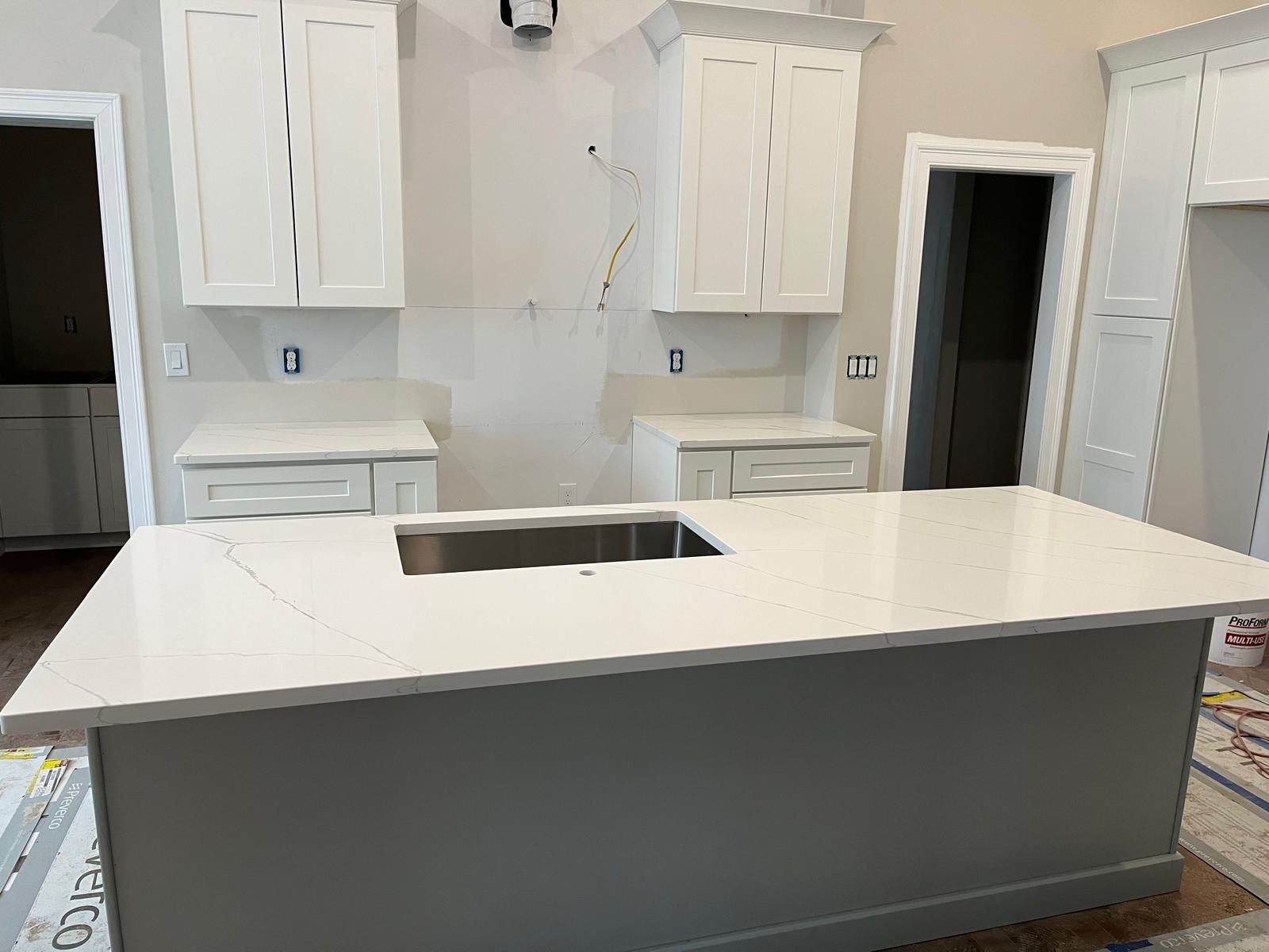 Kitchen with white cabinets, light gray island, and white countertop. A sink is set into the island.