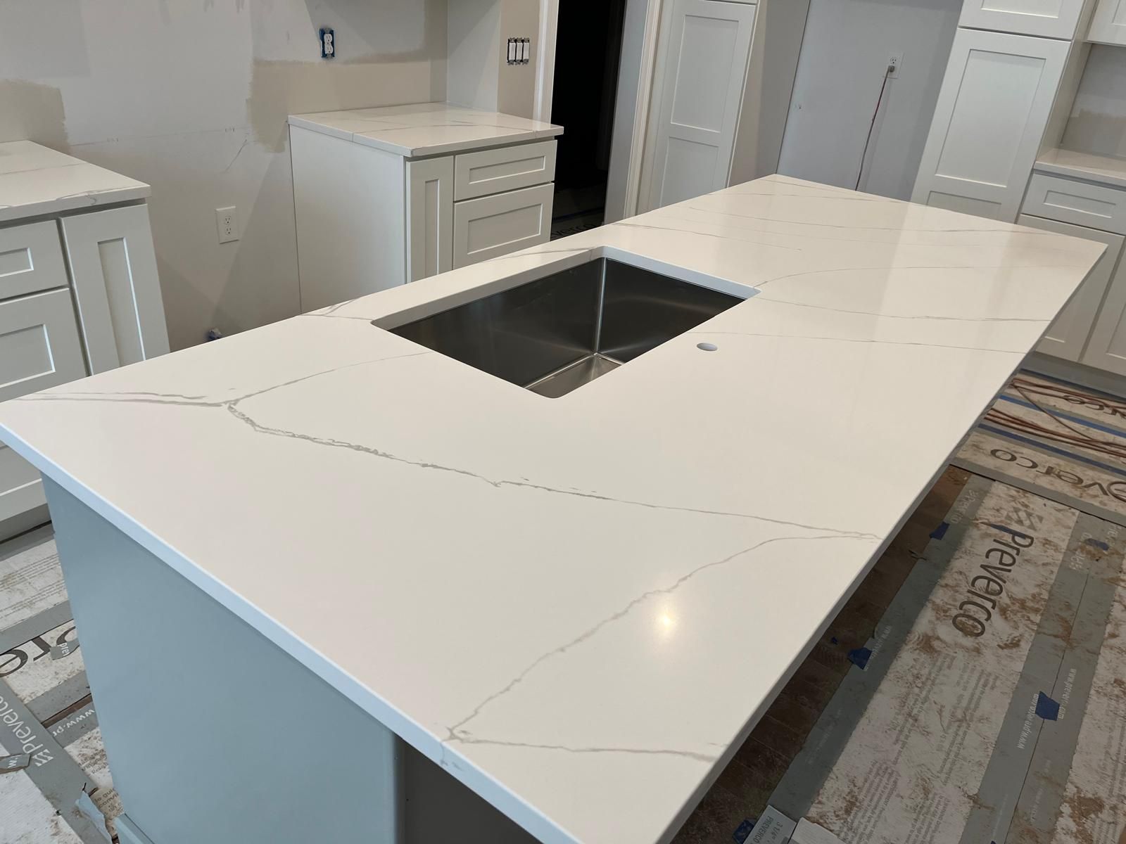 Kitchen island with white countertop, integrated sink, and light gray cabinetry.