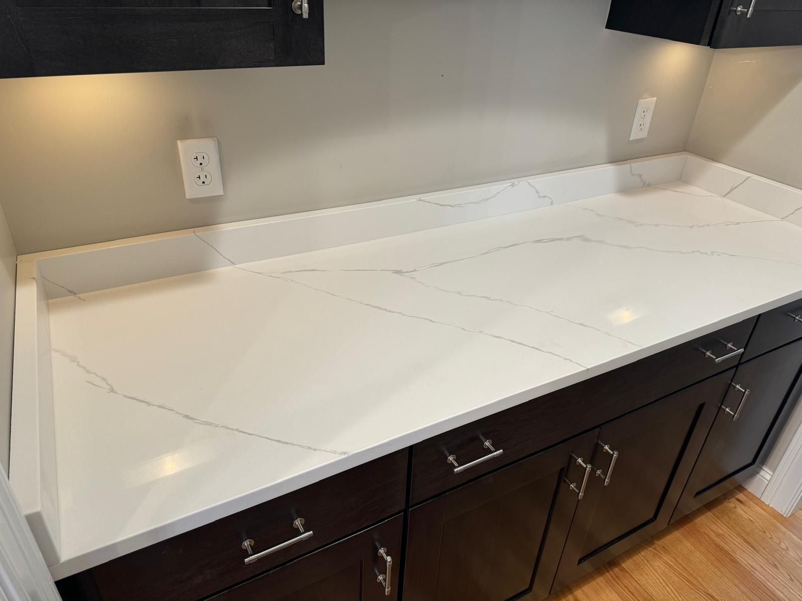 Kitchen with dark cabinets, white countertop with gray veining, and beige walls.