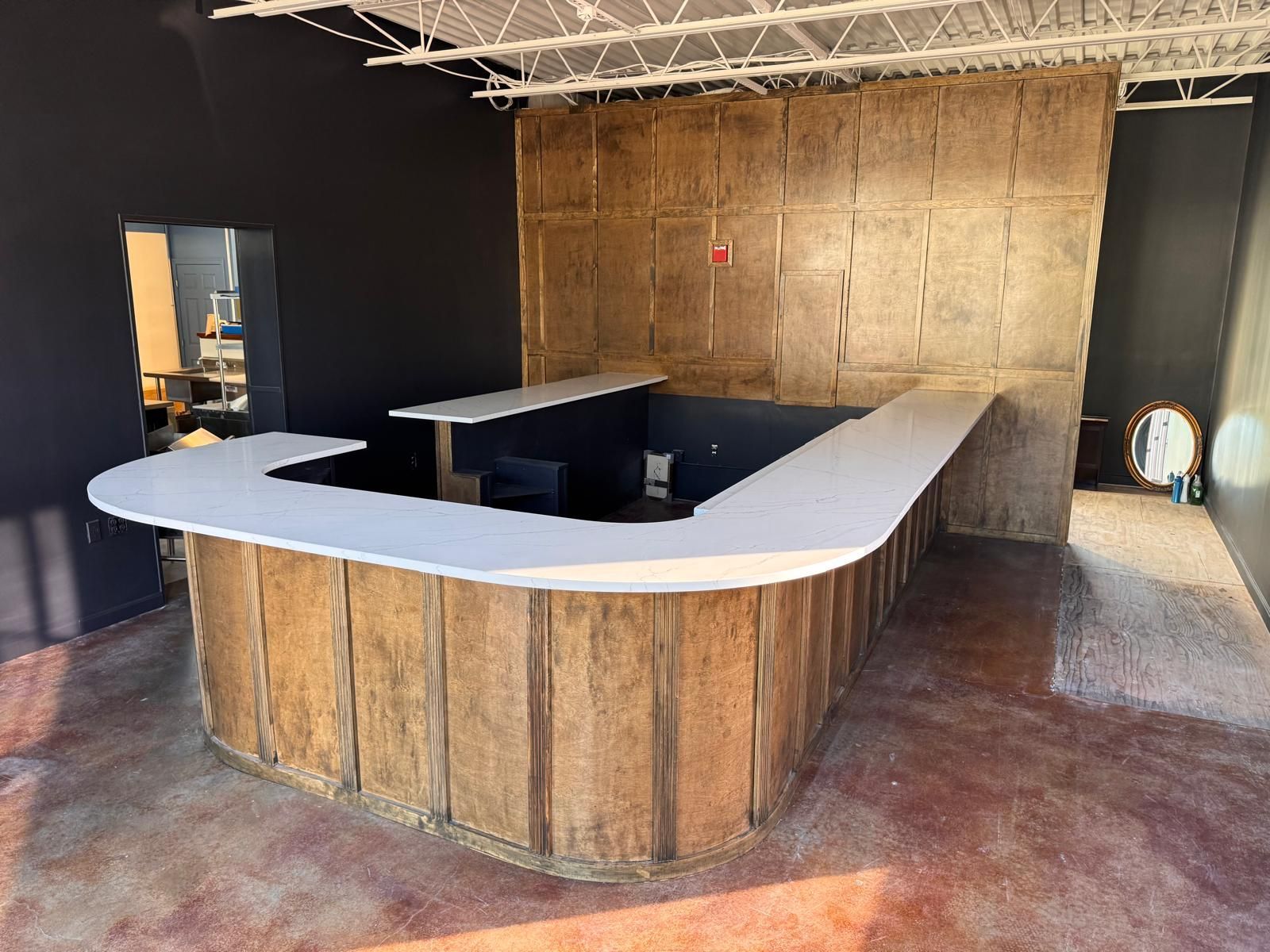 A U-shaped bar with a light countertop and wood-paneled base in a dark-walled room.