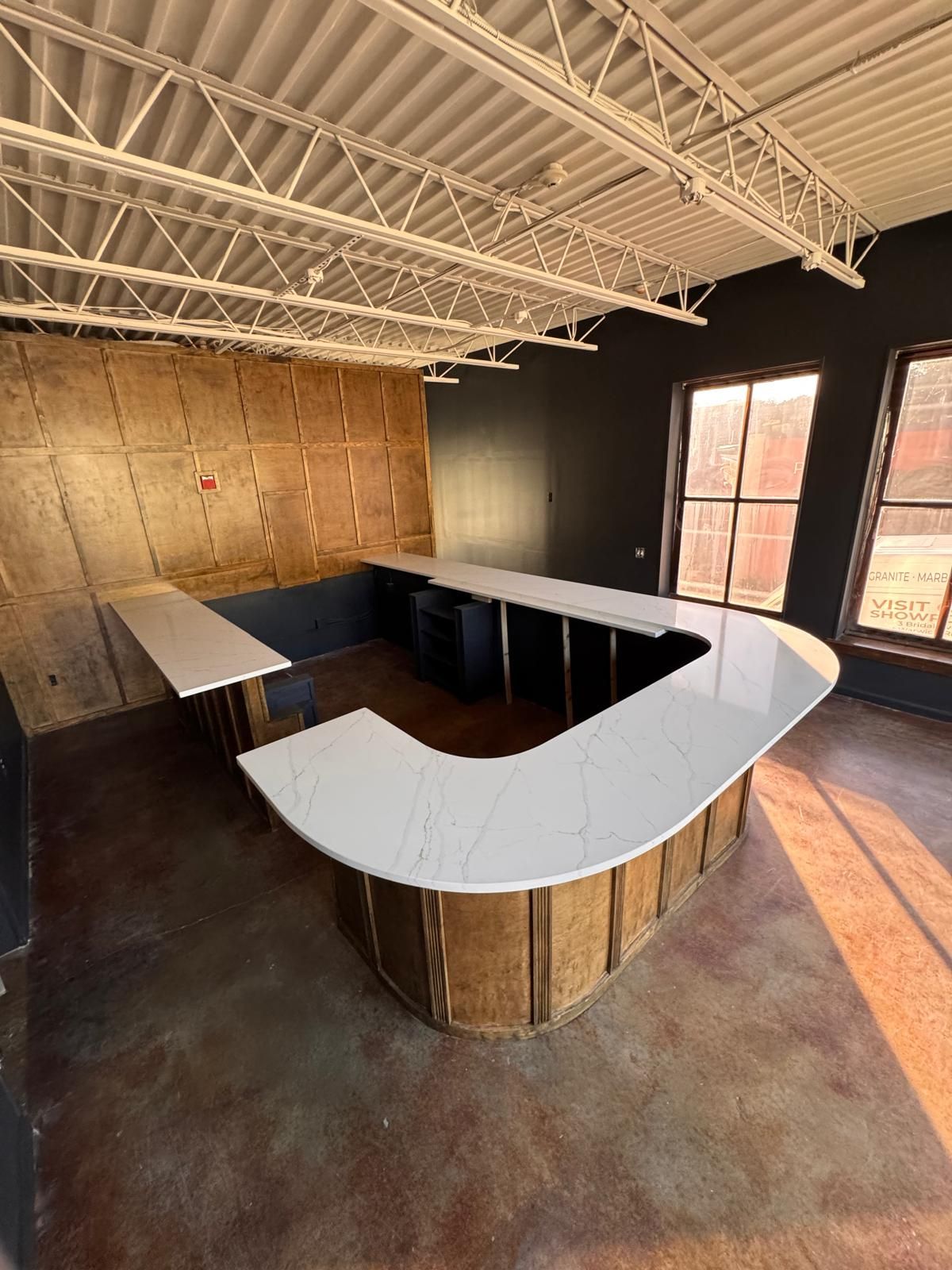 Empty bar with a curved white countertop and wooden base in a partially constructed room.