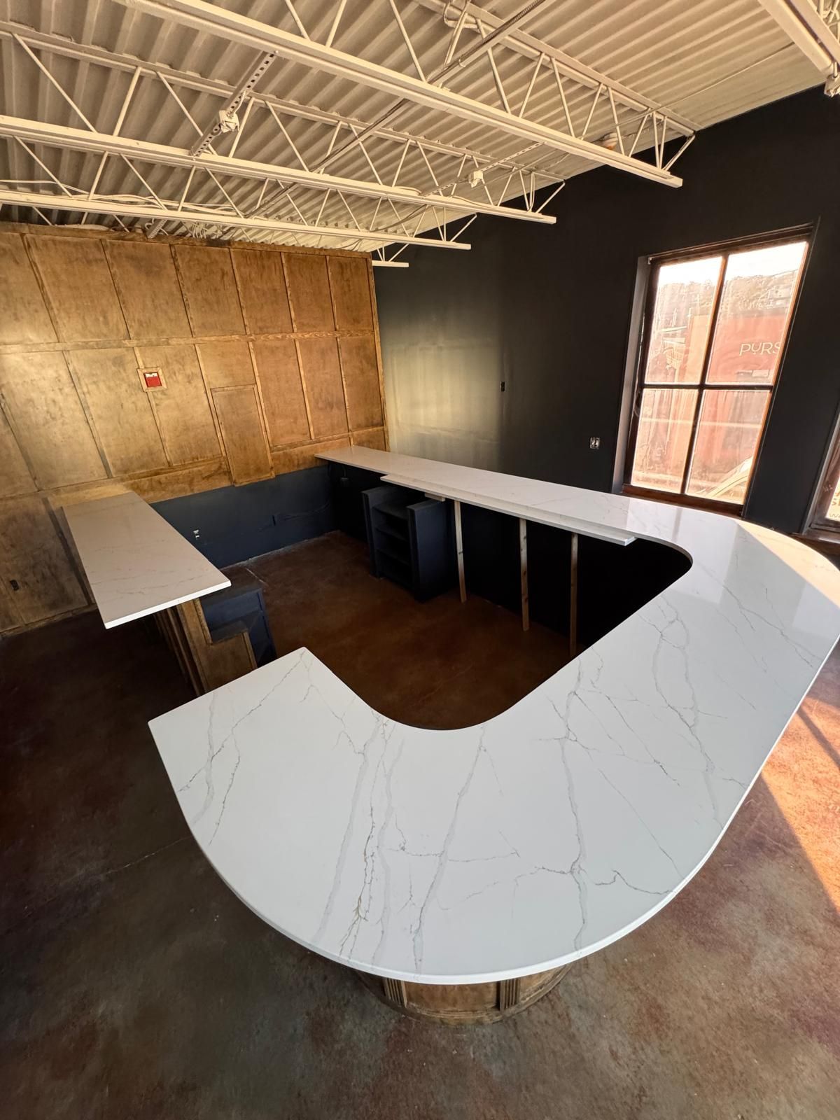 A large, white countertop with veining in a room under construction. The wall is dark gray with a window.