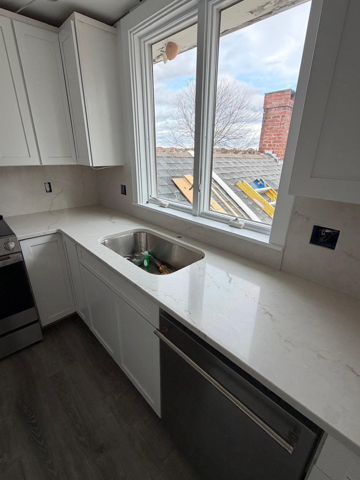 White kitchen with a countertop, stainless steel sink, window, and dishwasher.