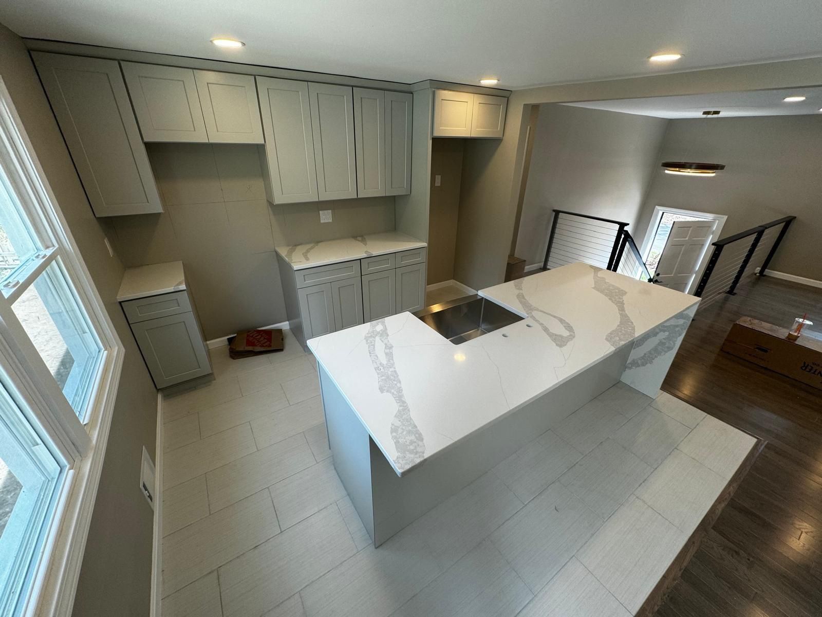 Modern kitchen with gray cabinets, white countertops, and large island with cooktop.