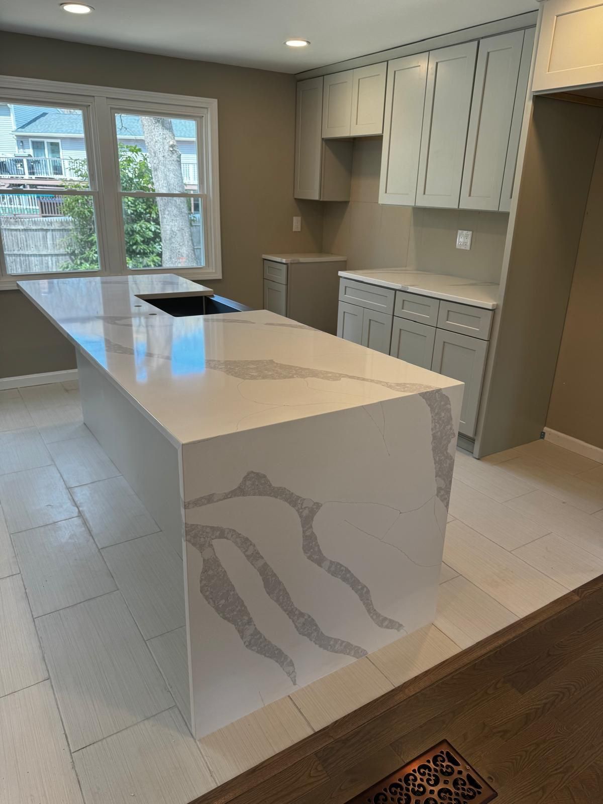 Modern kitchen with white quartz island, cabinets, and tile floor, window view.