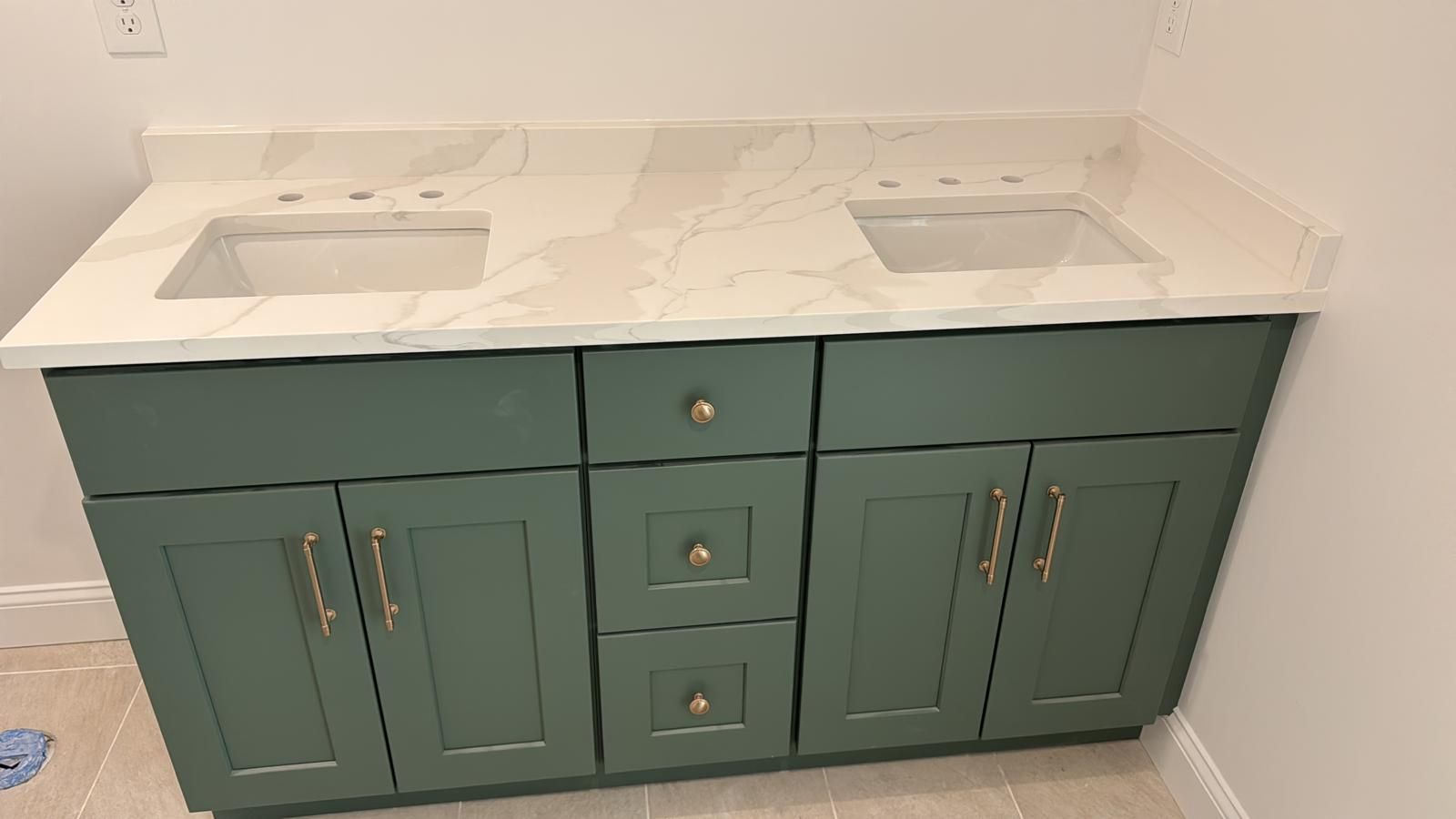 Green bathroom vanity with a white countertop and two sinks.