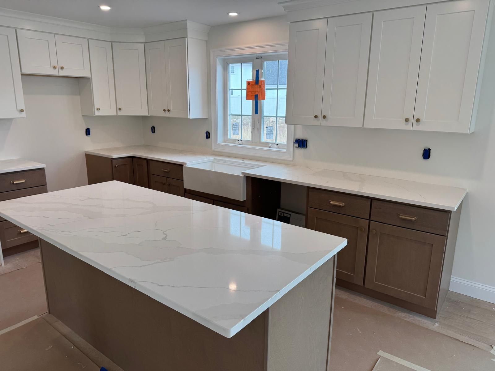 Kitchen with white upper cabinets, brown lower cabinets, and a white countertop island.