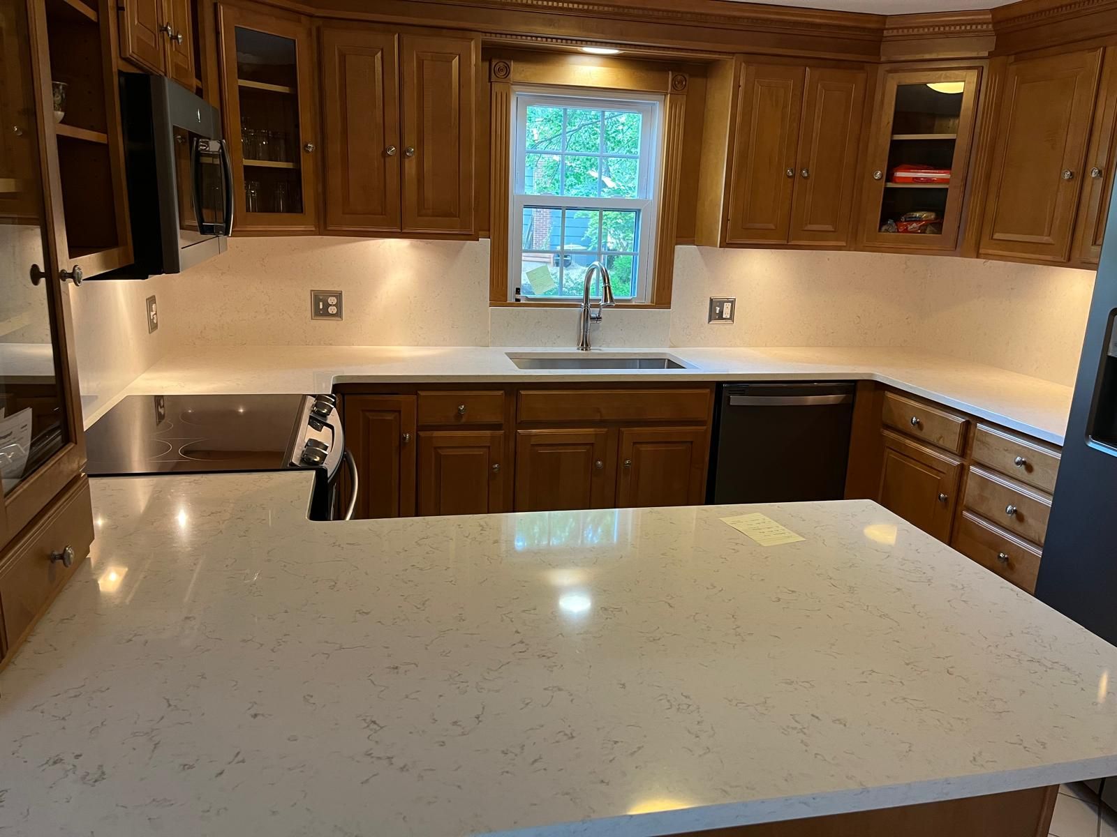 Kitchen with light countertops, wooden cabinets, and a sink beneath a window.