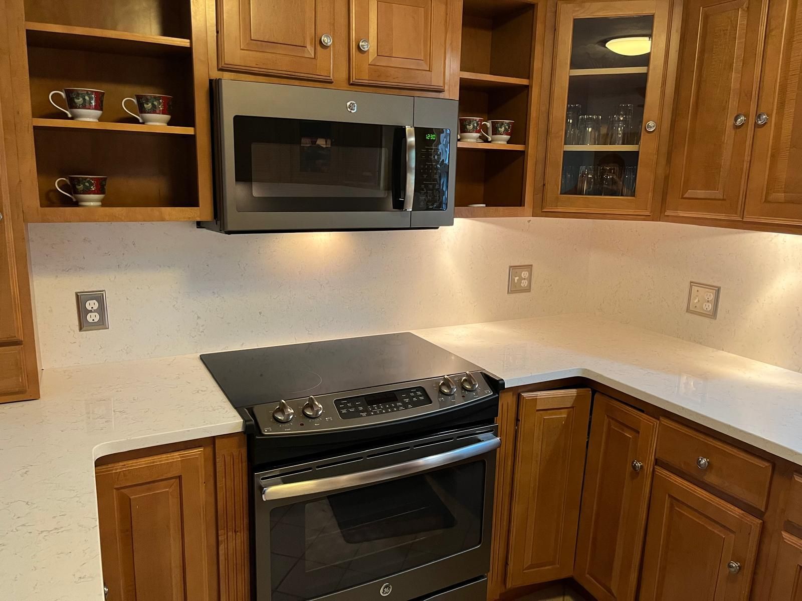 A kitchen with wooden cabinets, a stovetop, microwave, and white countertops.