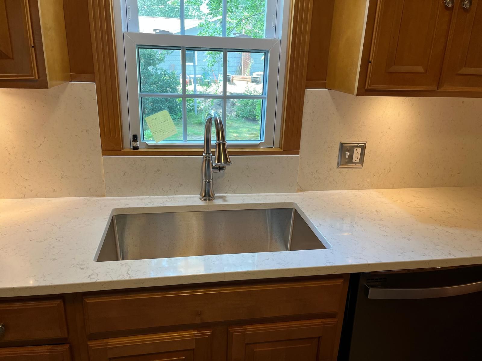 Kitchen with a stainless steel sink, white countertops, and wooden cabinets.