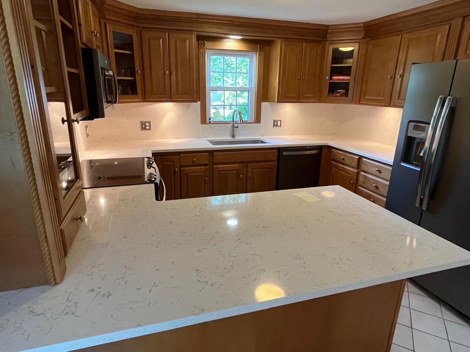 Kitchen with light quartz countertops, wooden cabinets, and a stainless steel refrigerator.