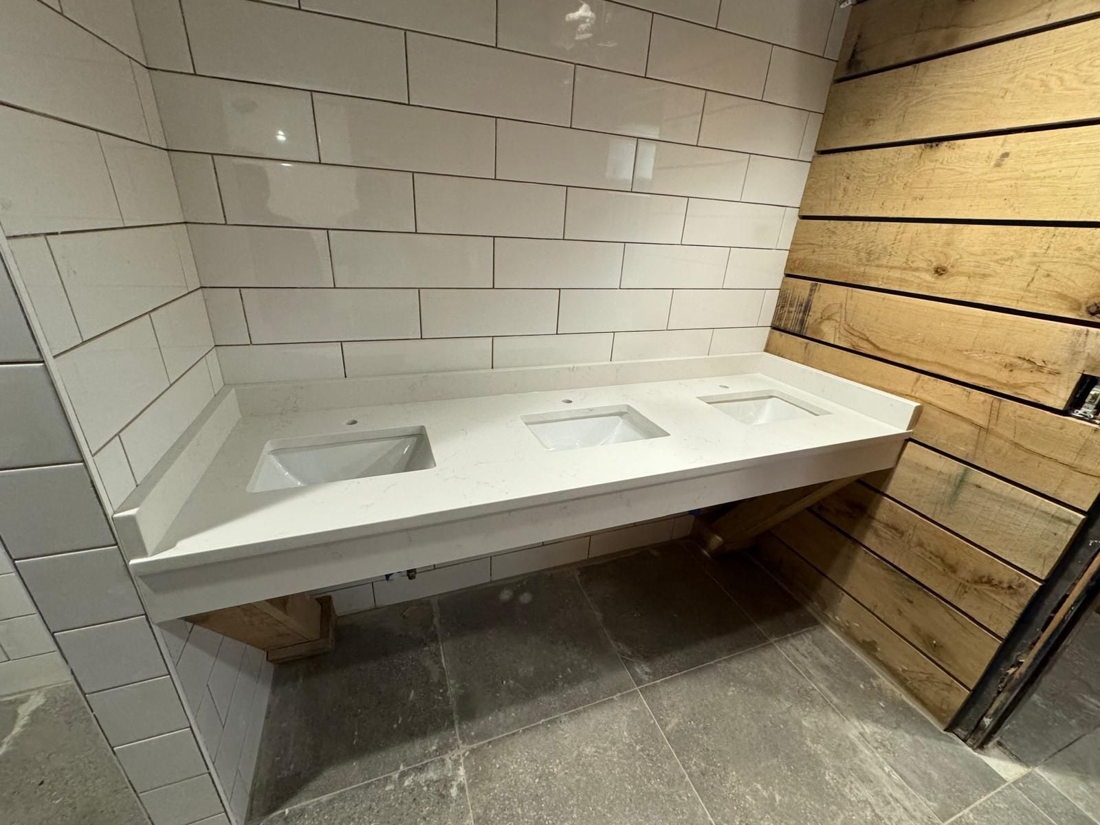 White countertop with three sinks against white tiled and wood-paneled walls.