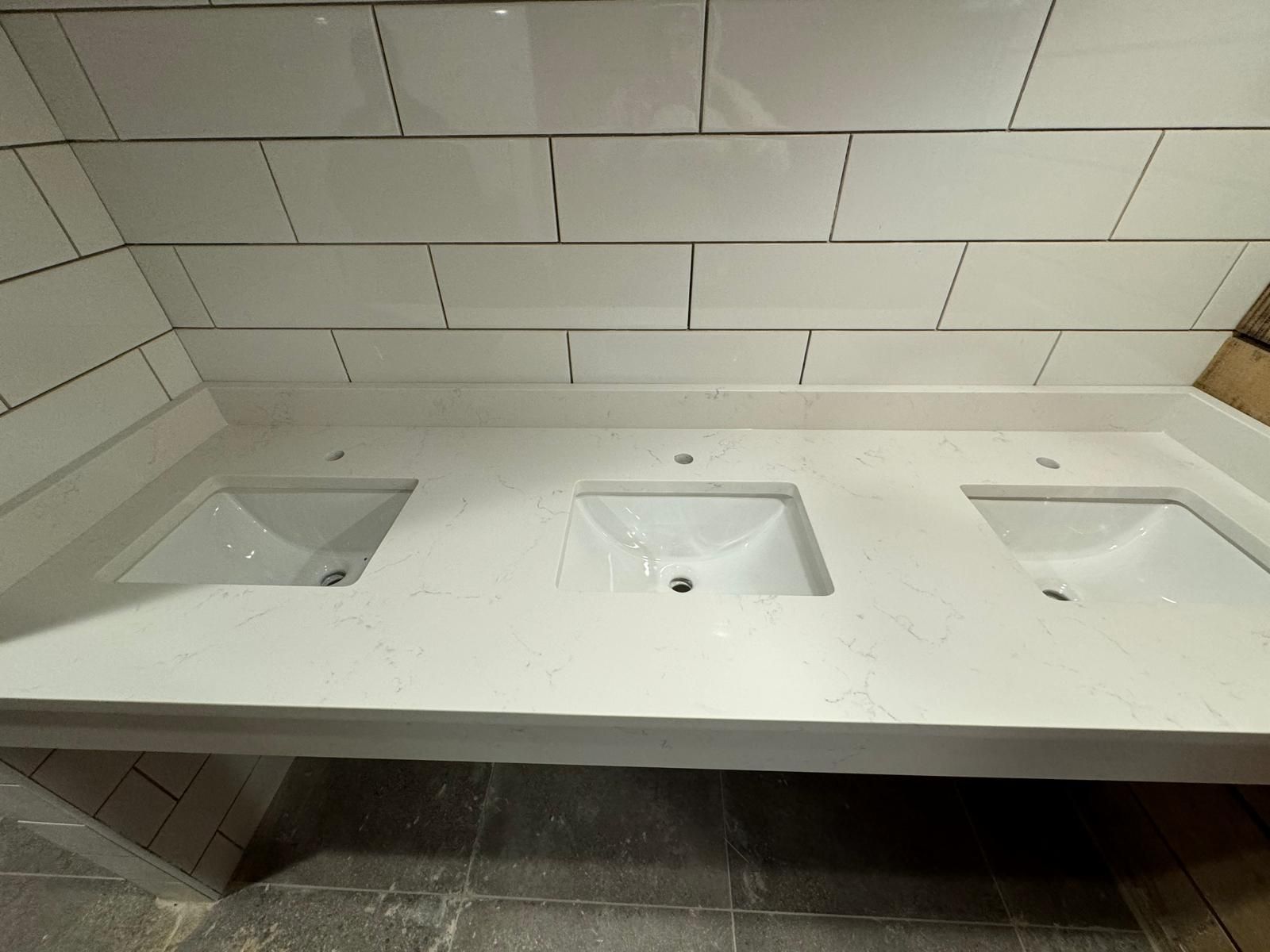 White bathroom vanity with three sinks, tile backsplash, and light gray counter.
