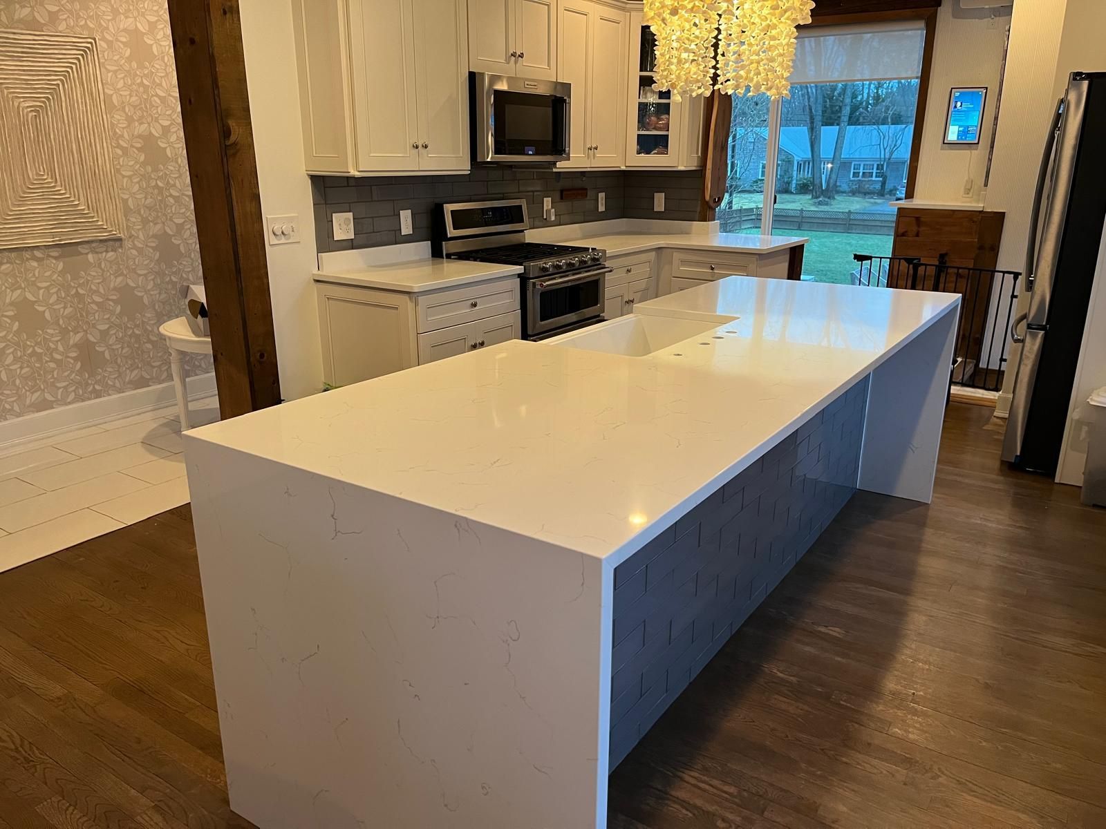 Modern kitchen with white countertops and gray cabinets. Large island in foreground.