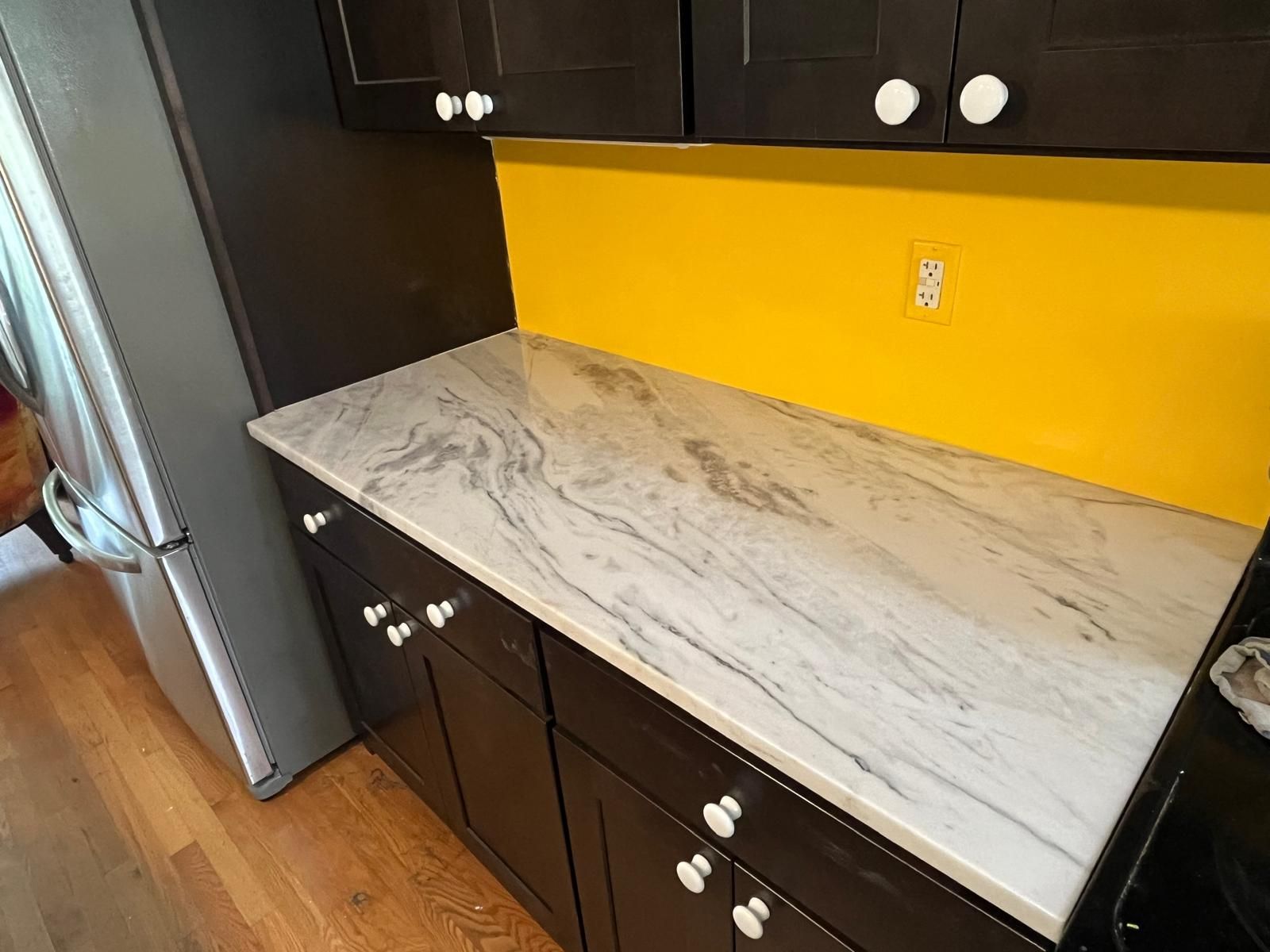 Kitchen counter with gray and white marbled surface, black cabinets, and yellow backsplash.