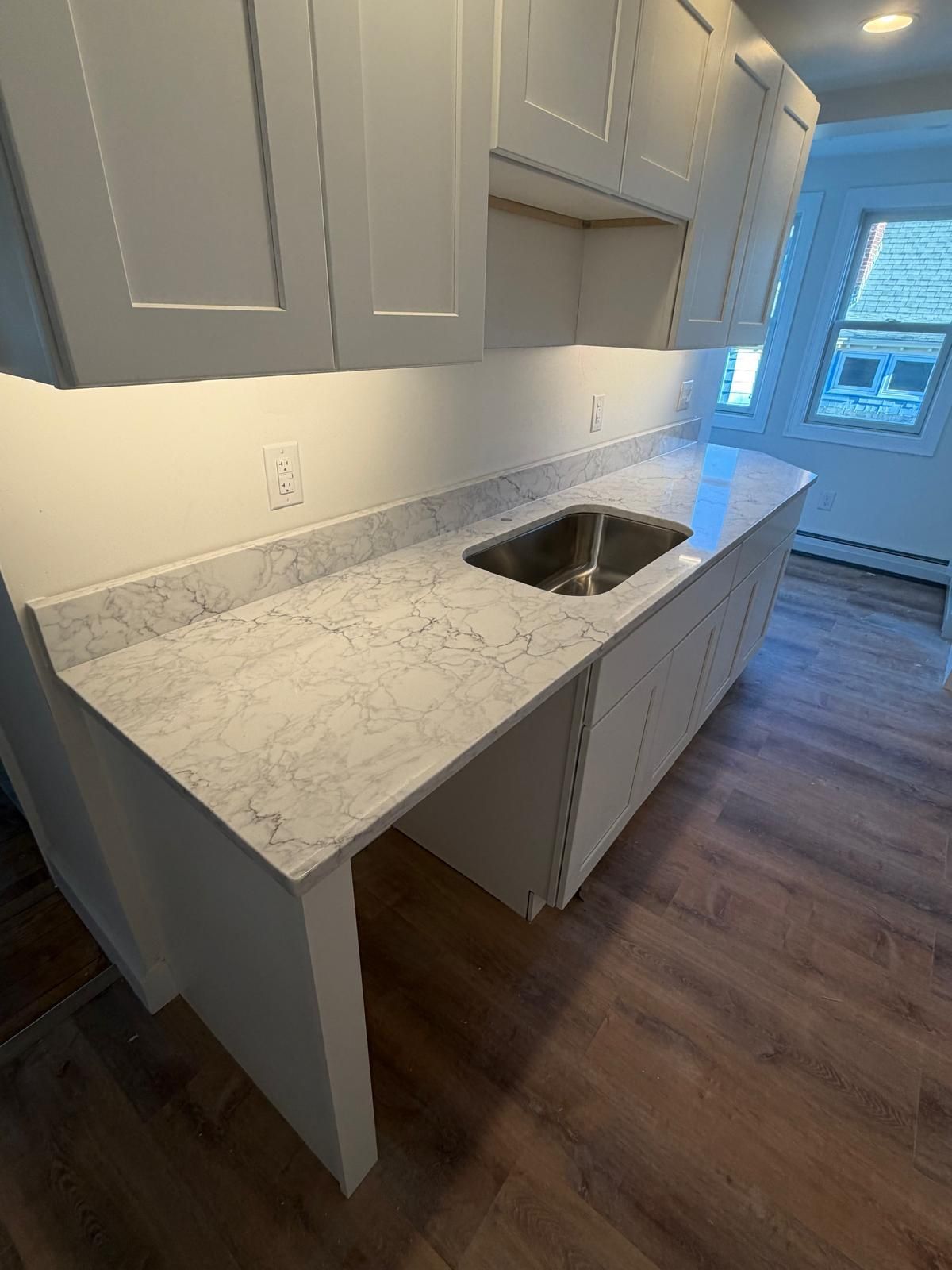 White kitchen cabinetry with a light gray countertop and a stainless steel sink.