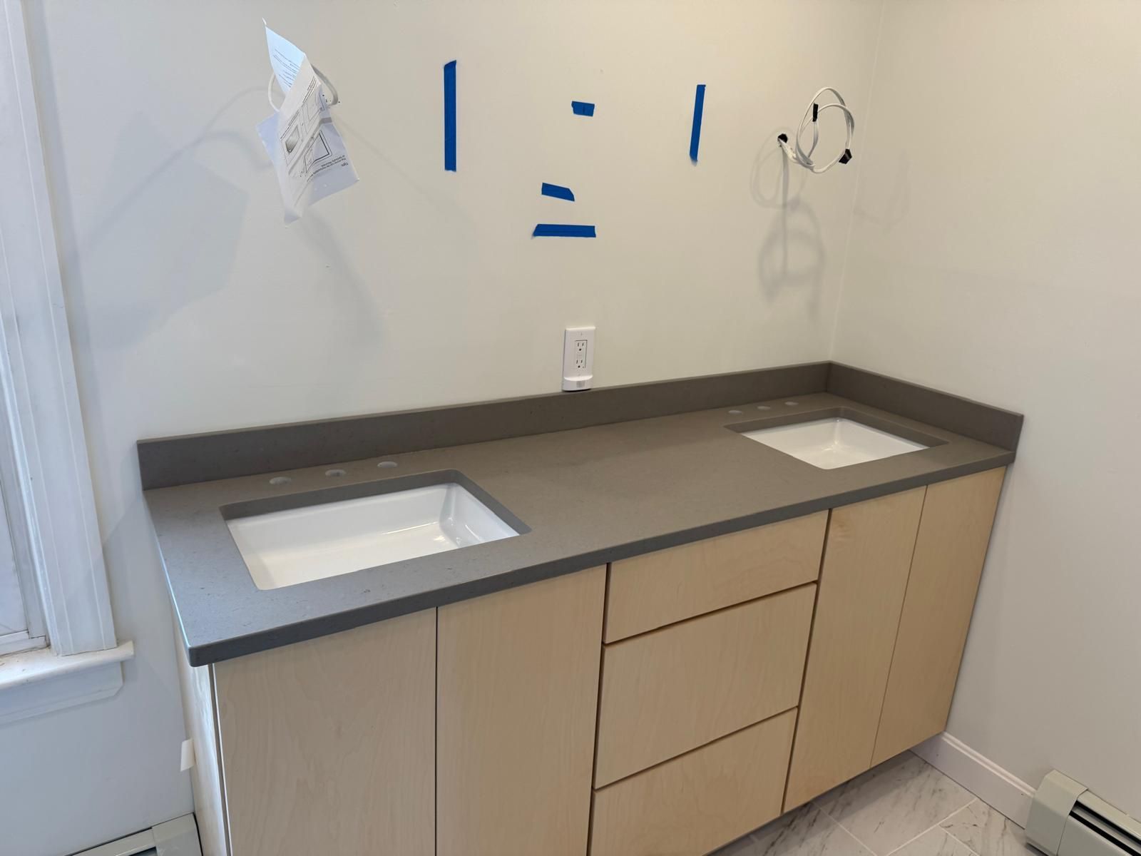 Bathroom vanity with two sinks, gray countertop, light wood cabinets, and white walls.