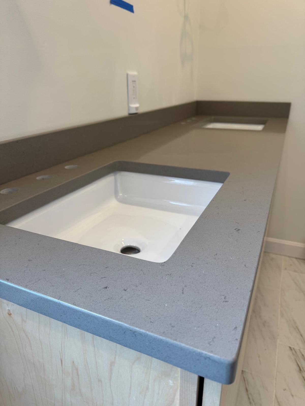 Gray countertop with a rectangular sink, set in a light wood cabinet, near a white wall and an electrical outlet.